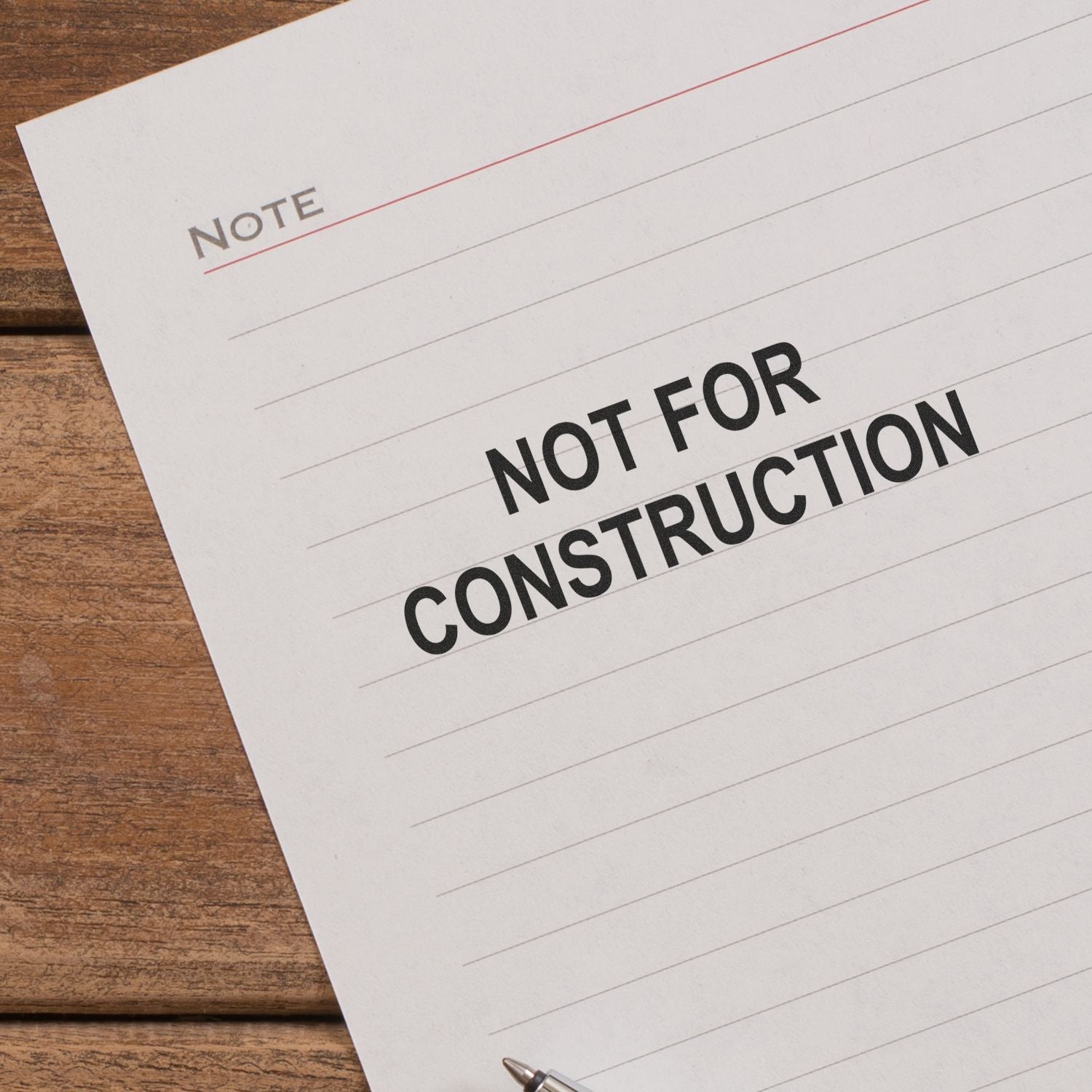 Not for construction note on lined paper on a wooden desk with pen.