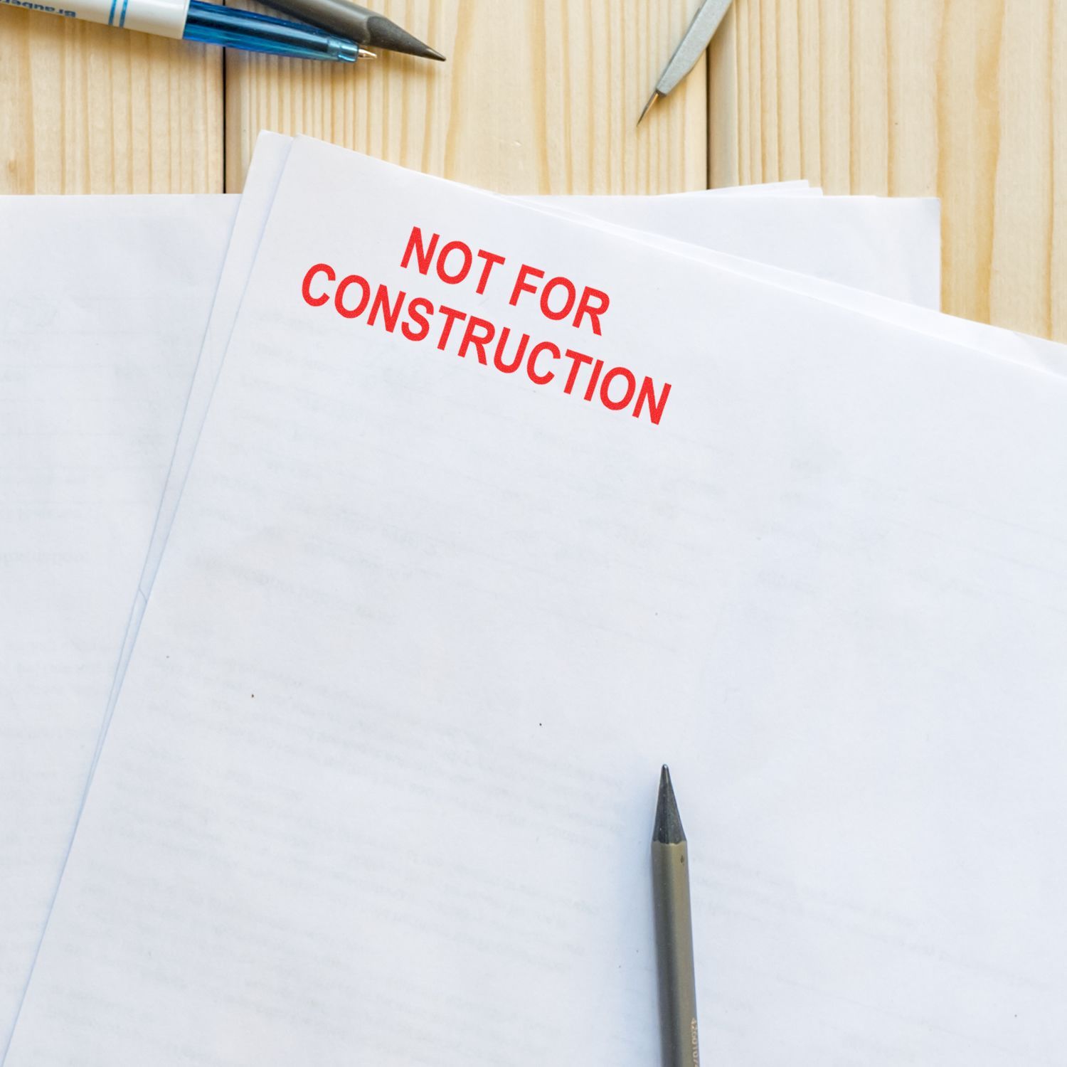 Not for Construction stamped on architectural plans with pens on a wooden desk, concept for building permit and design review.