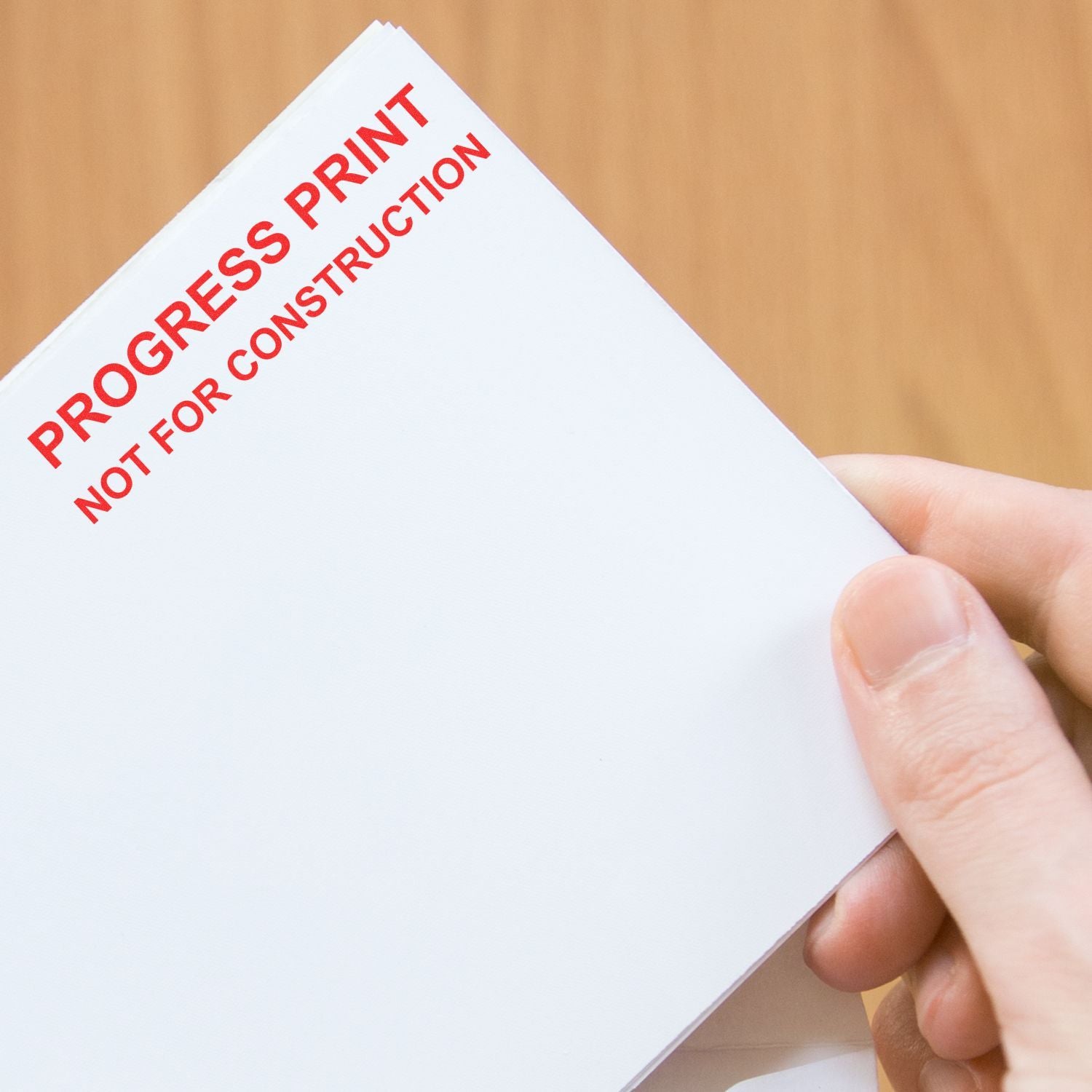 Hand holding a progress print document labeled Not for Construction on a wooden background.