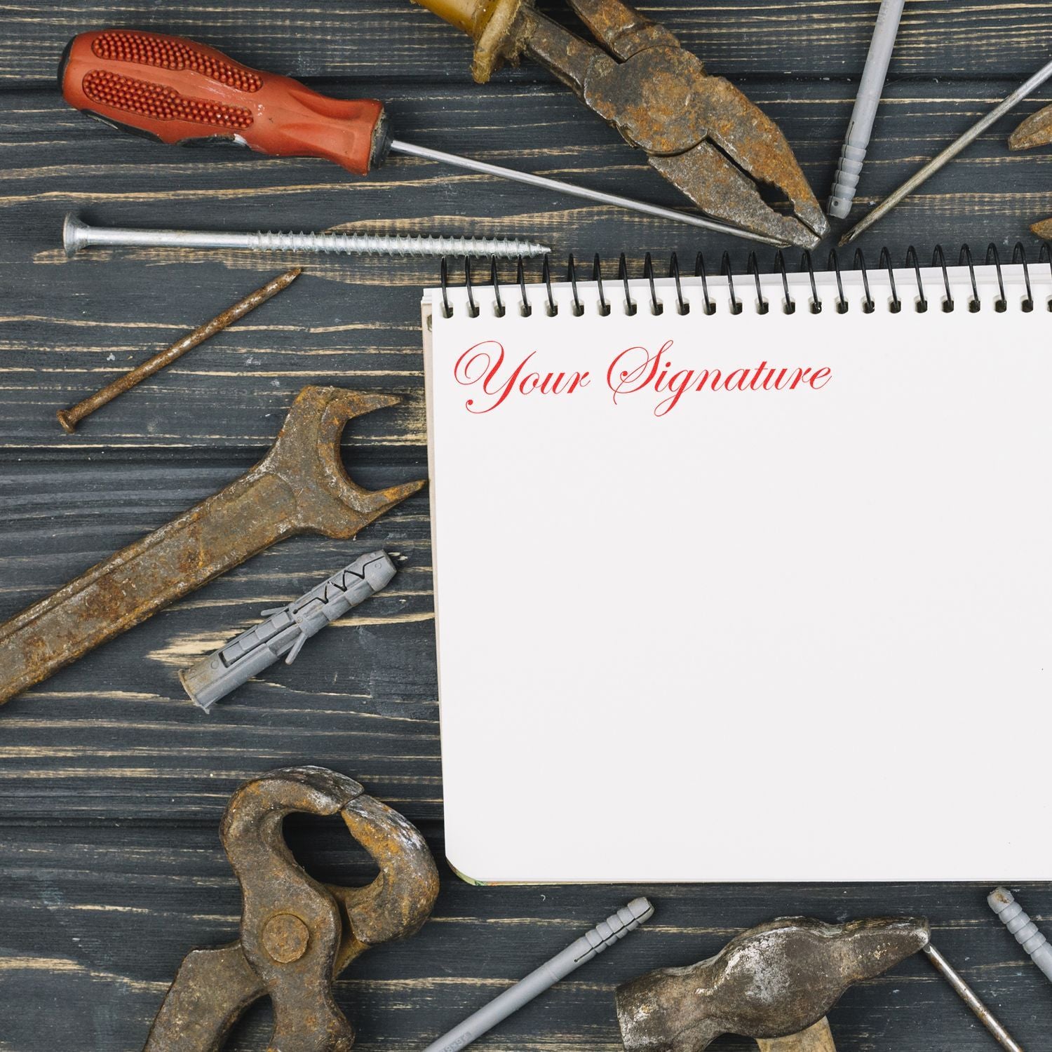 Rusty hand tools and screws around a spiral notebook with Your Signature on a dark wooden background.