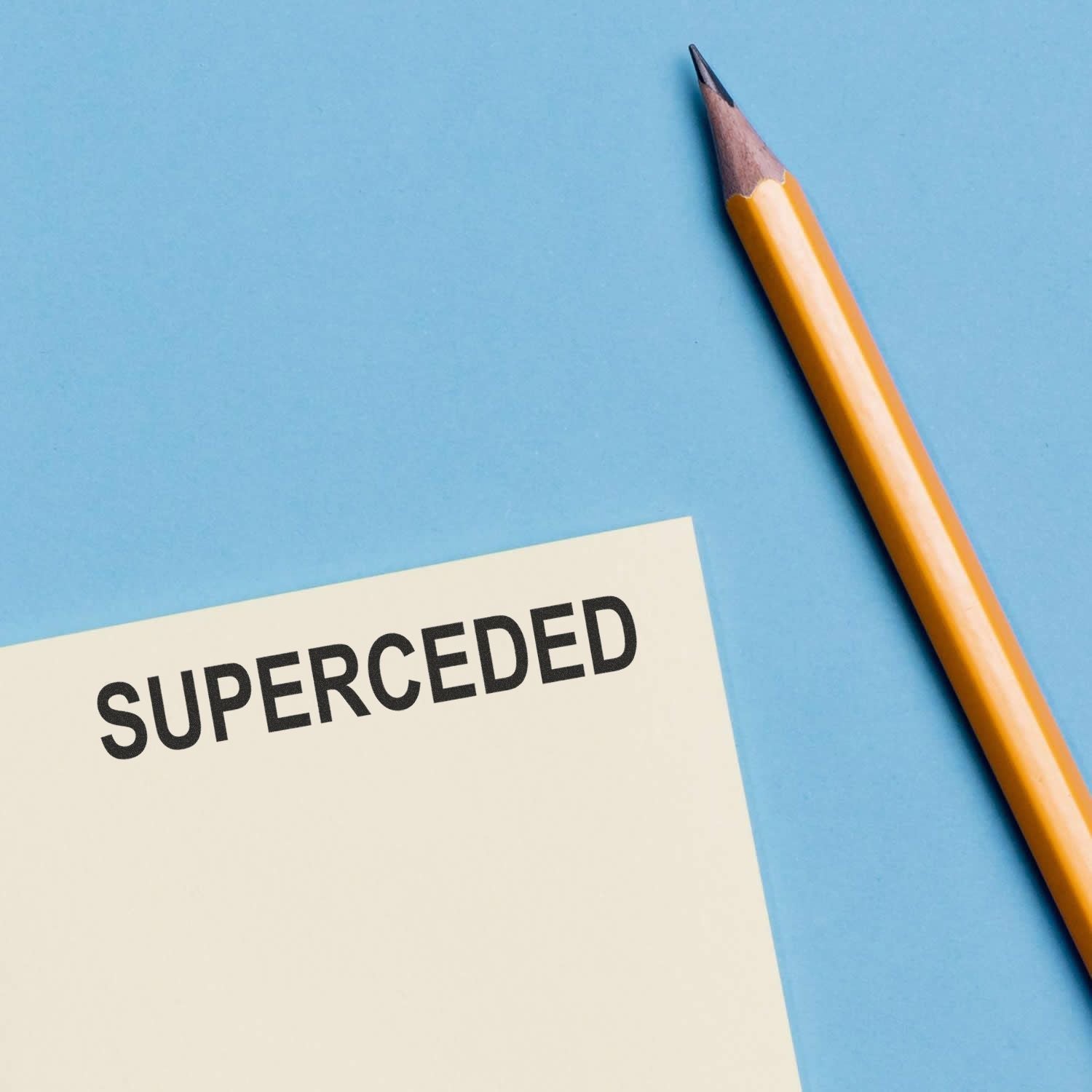 Yellow pencil beside a note labeled superceded on a blue background, business concept image.