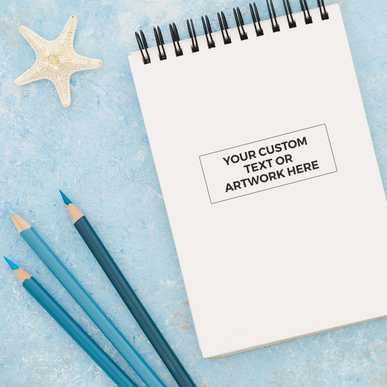 Customizable notebook mockup with Your Custom Text or Artwork Here, blue background, pencils and starfish for beach design branding