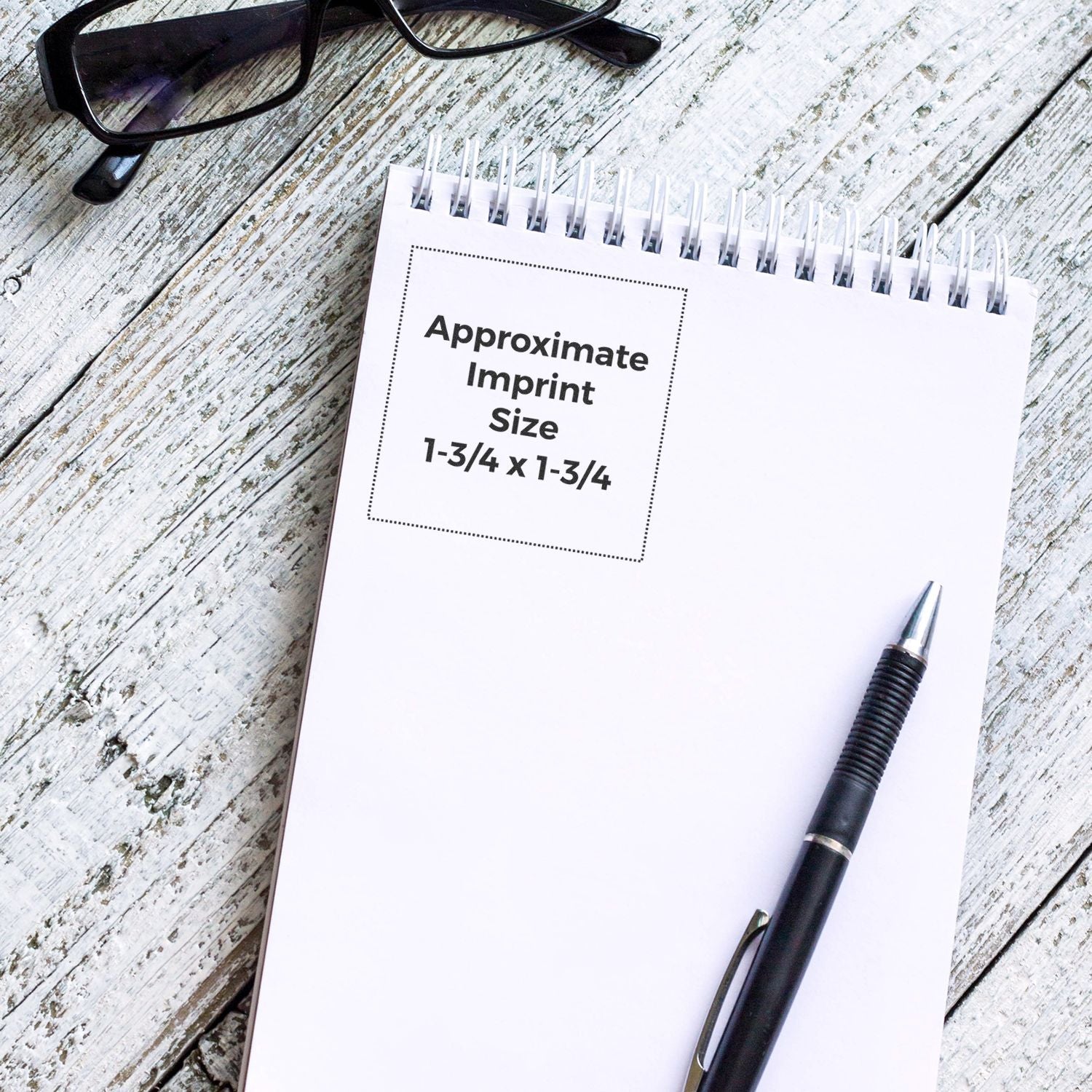 Notebook mockup showing approximate imprint size 1-3/4 x 1-3/4 for custom logo branding, with pen and eyeglasses.