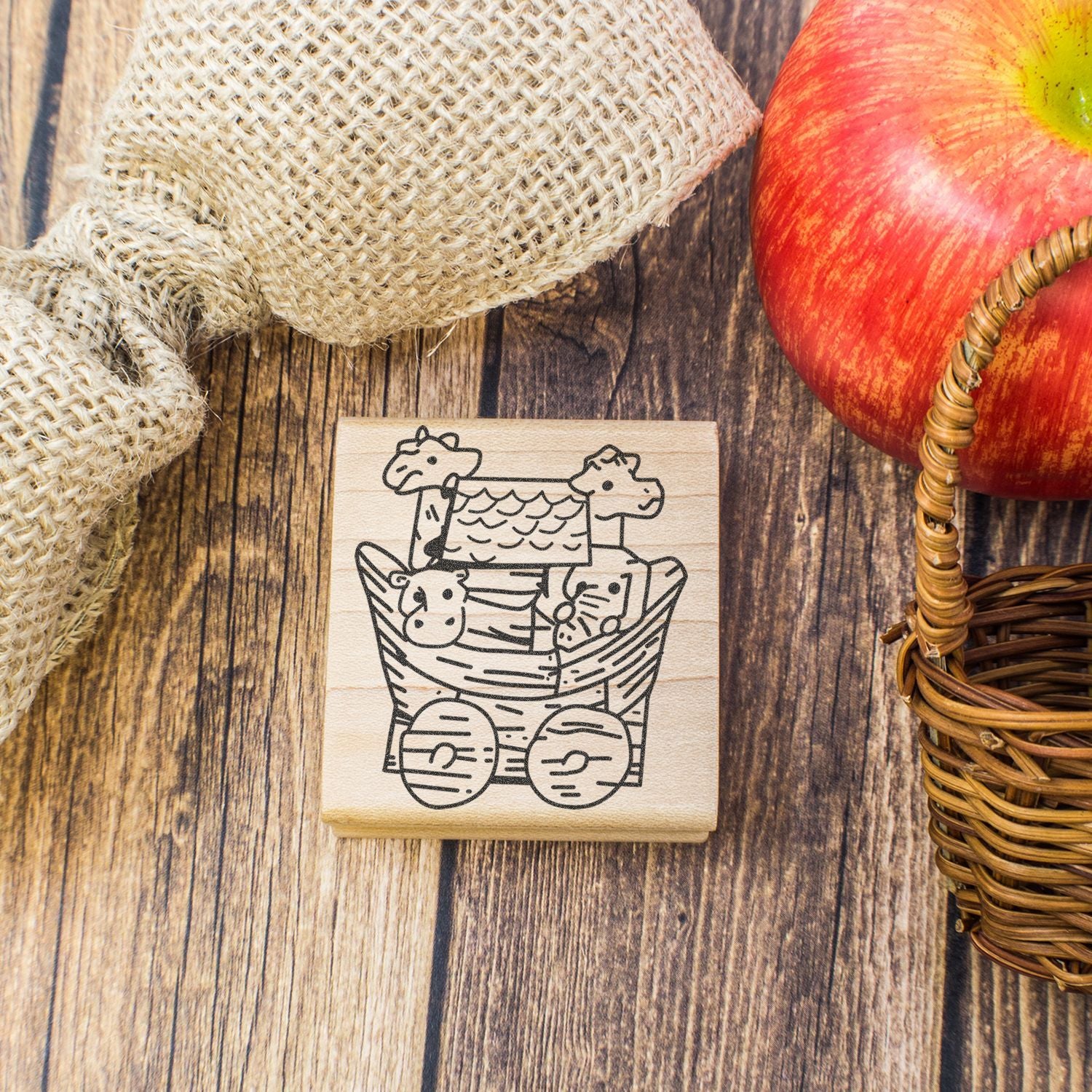 Rustic autumn flat lay with apple, burlap, wicker basket, and wooden farm animal stamp on a wood table