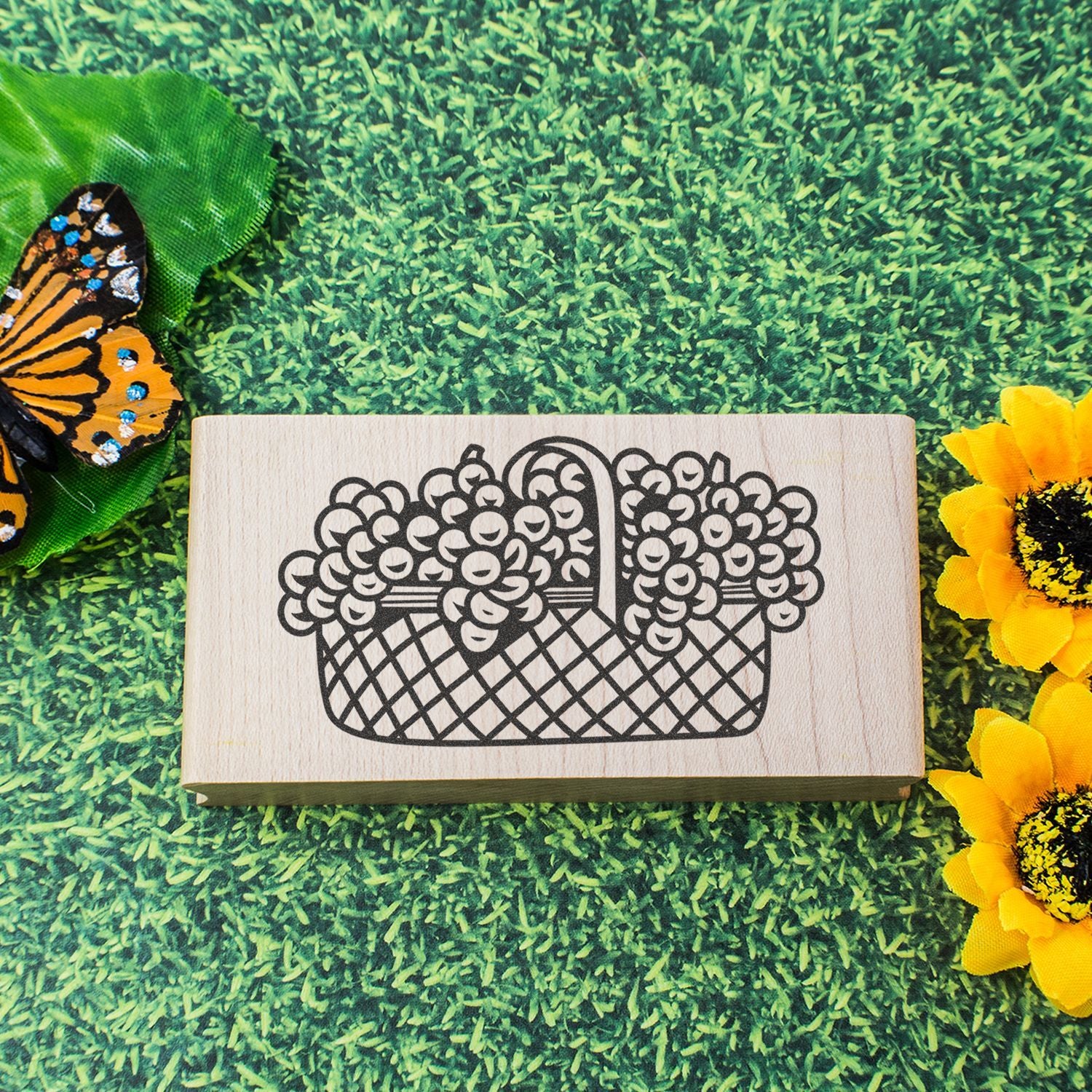 Rustic wooden stamp with basket of berries illustration on green grass, with butterfly and sunflower accents.