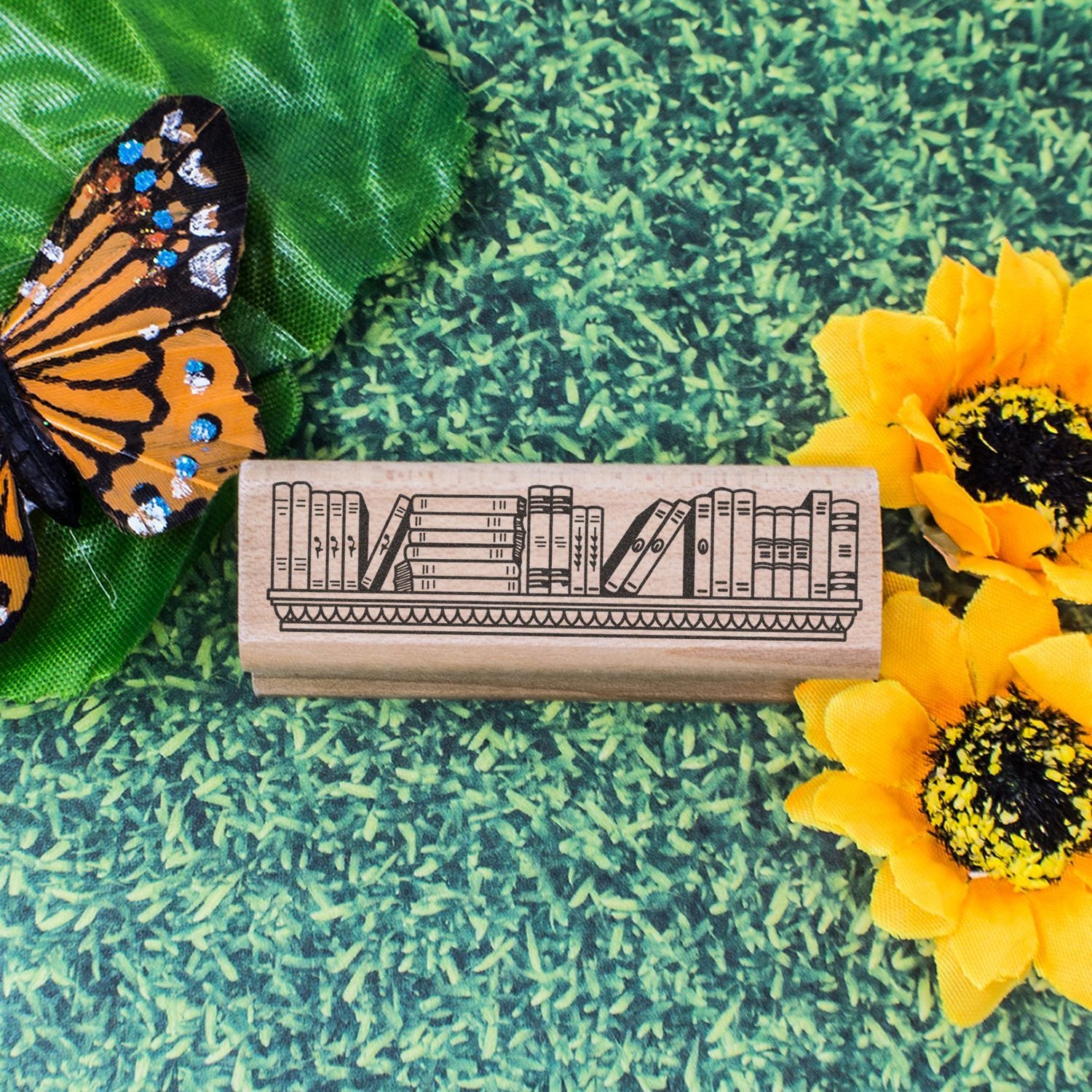 Decorative wooden bookshelf stamp with butterfly and sunflowers on a green textured background