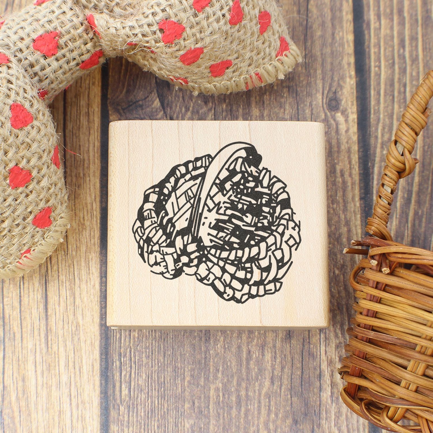 Wooden rubber stamp with abstract black floral design on rustic wood background, surrounded by woven fabric and wicker decor.