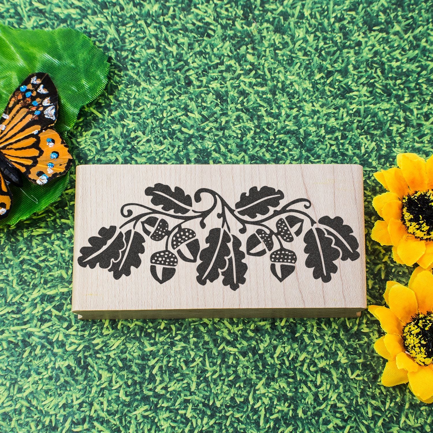 Wooden oak leaf and acorn stamp block on grass with butterfly and sunflower decor, rustic nature craft design.