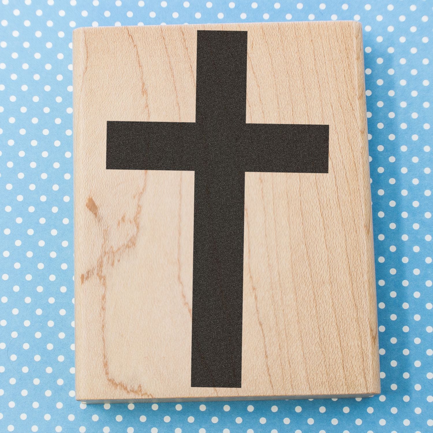 Wooden block with black cross on blue polka dot background, simple Christian symbol design.