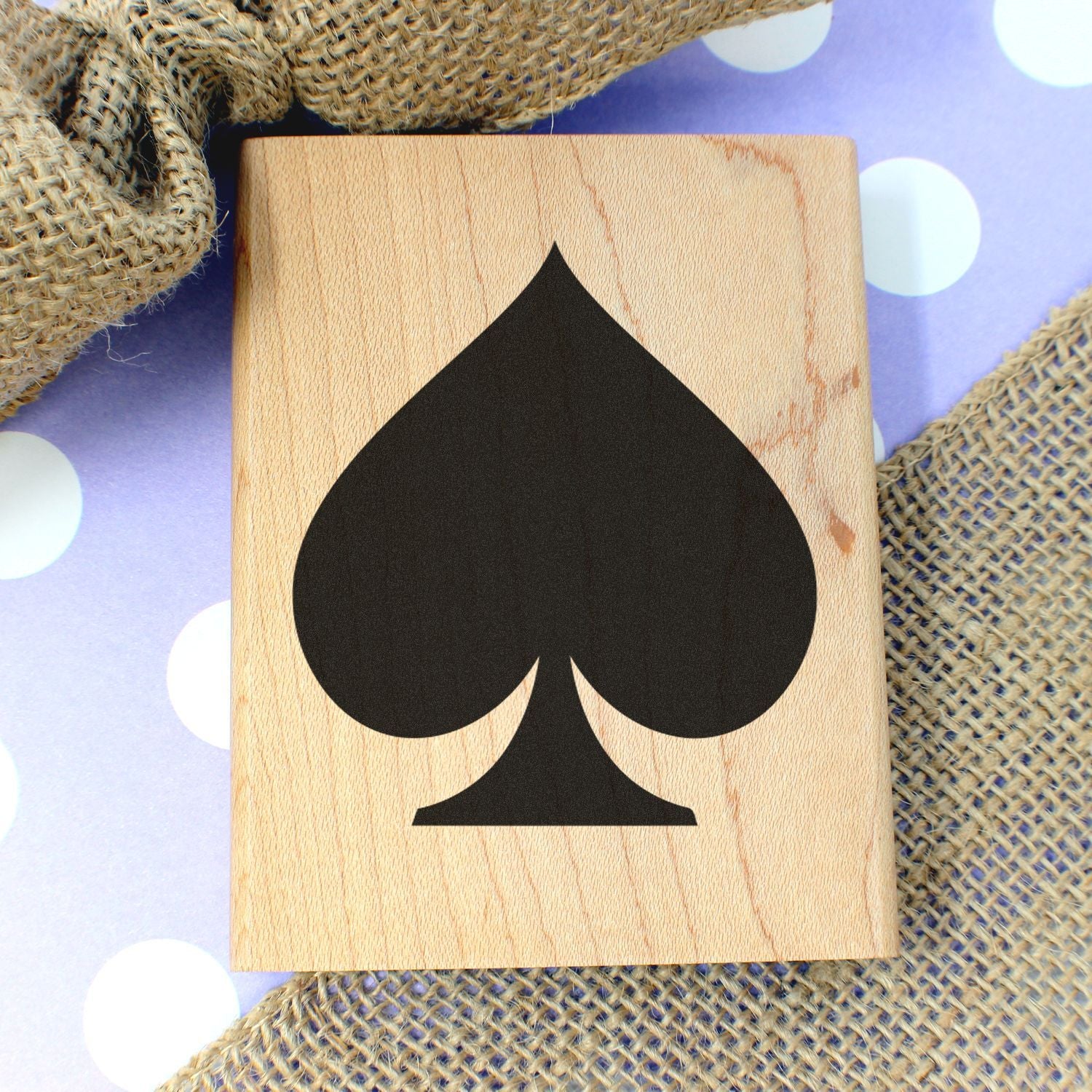 Black spade symbol on a wooden block with burlap and polka dot background, playing card suit design.