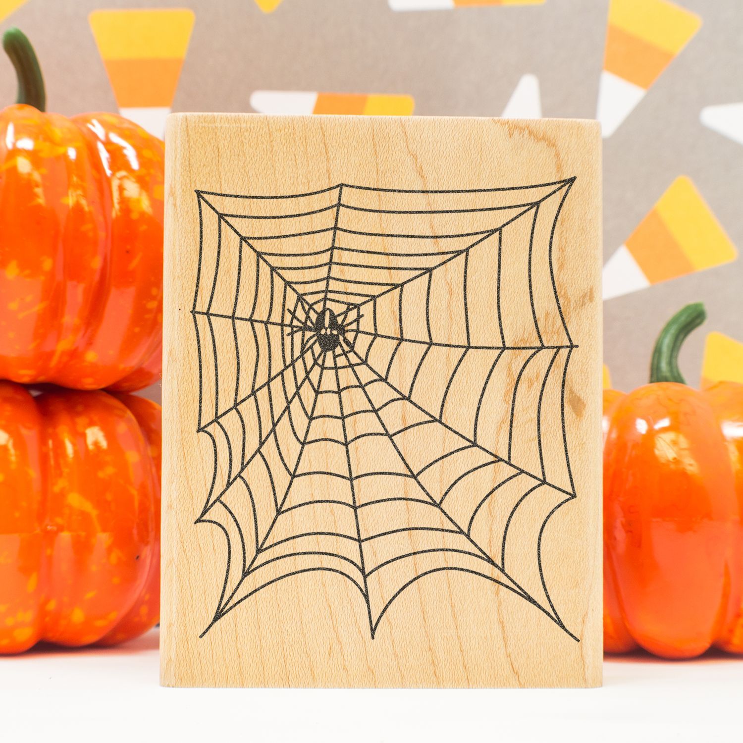 Wooden Halloween block with spider web design surrounded by orange pumpkins and fall decor.