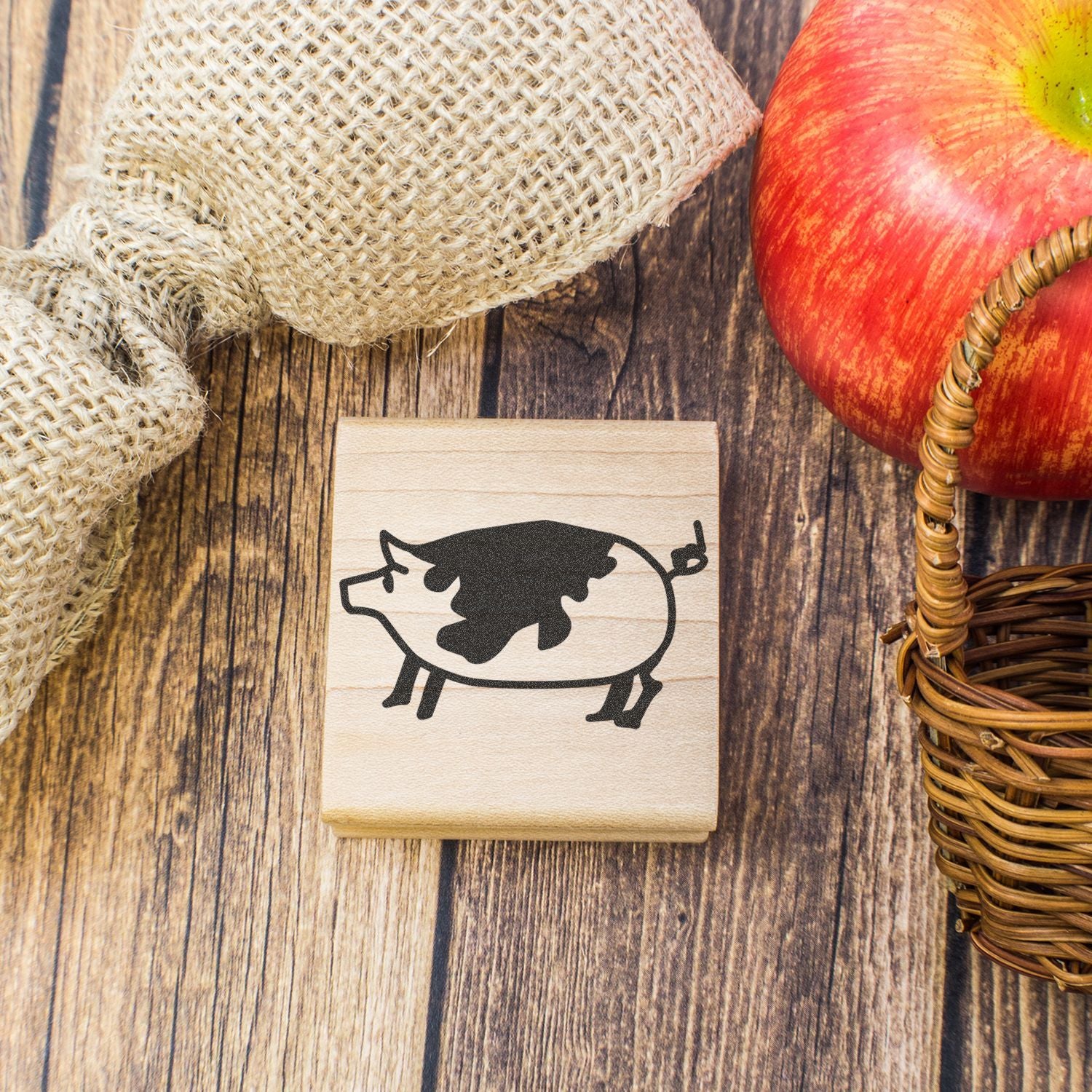 Rustic wooden stamp with pig silhouette, red apple, and wicker basket on farmhouse wood background