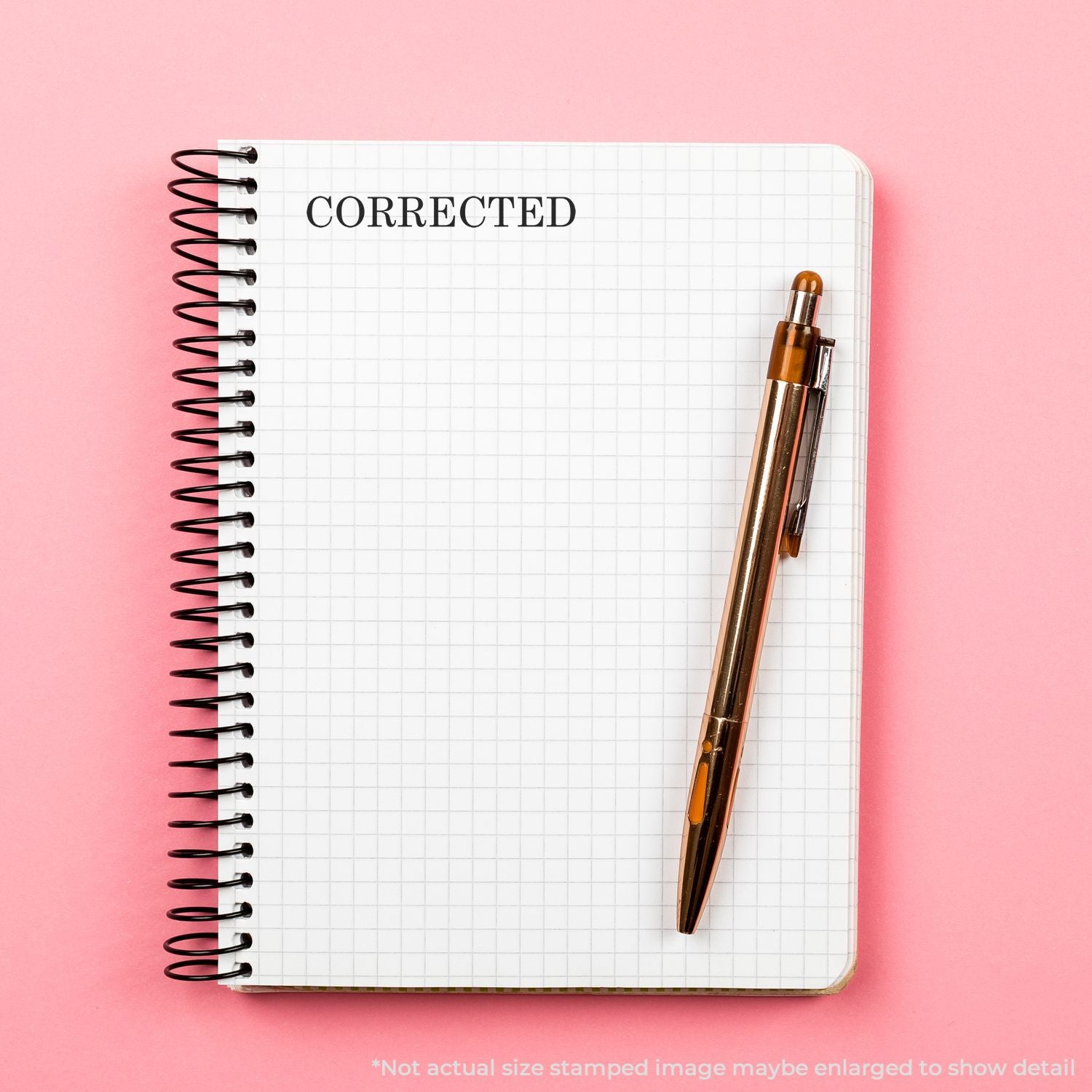 Spiral notebook with CORRECTED text and pen on a pink background