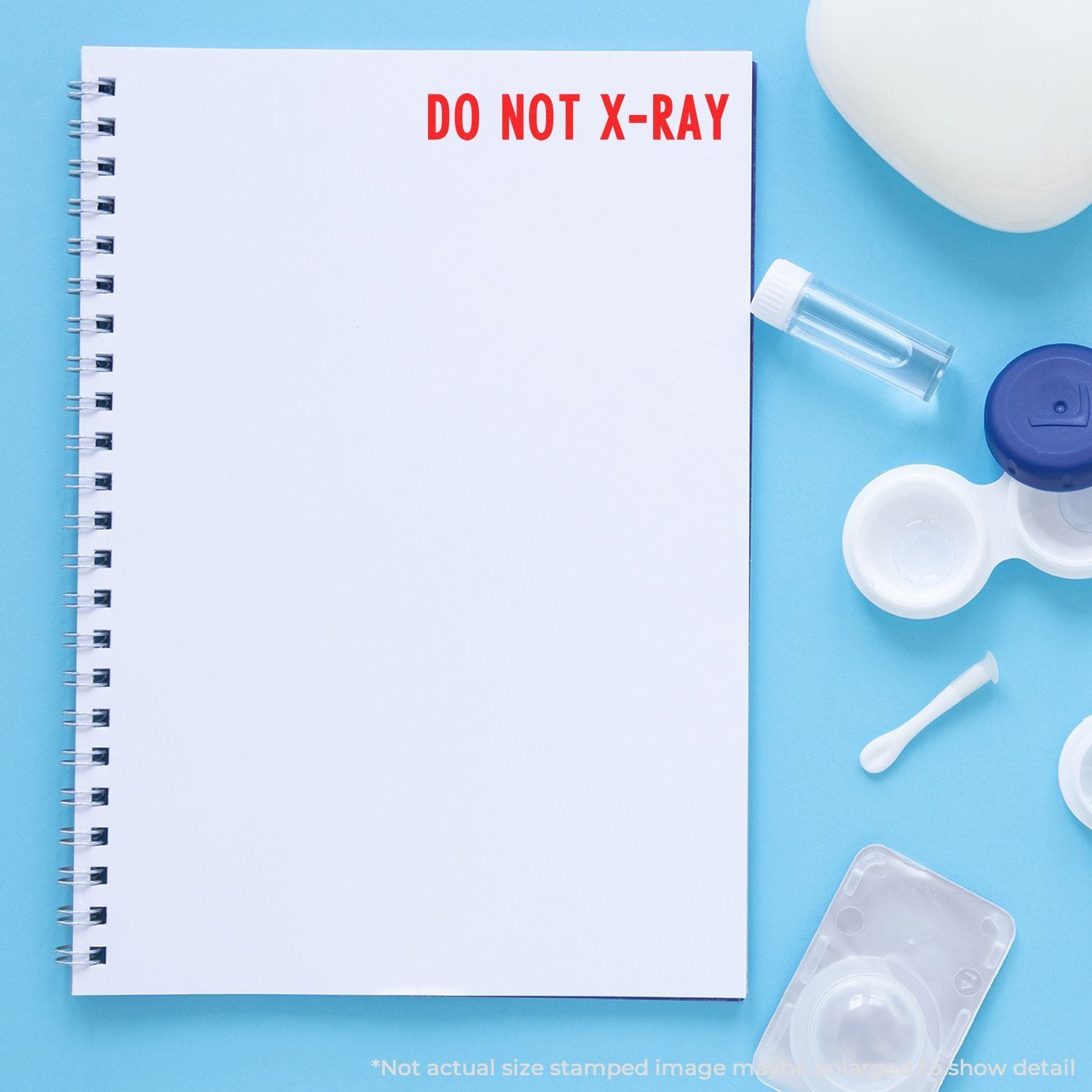 Blank spiral notebook stamped Do Not X-Ray with contact lens case, solution vial, and eye care accessories on blue background.