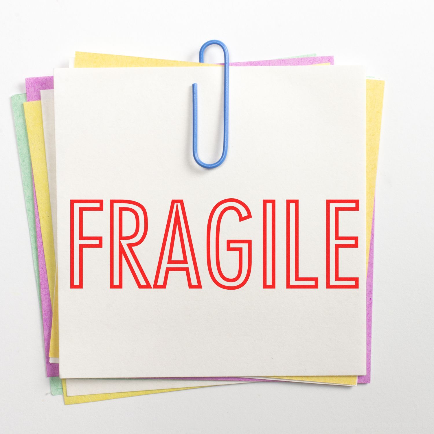 FRAGILE warning on a stack of stationery notes held by a blue paperclip, conveying shipping care for breakable items.