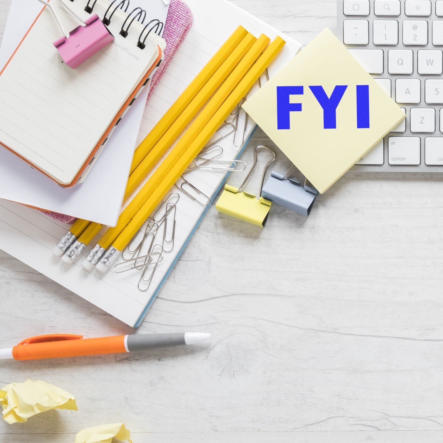 Office desk with notebook, pencils, paper clips, keyboard, and FYI sticky note for business planning or office organization.