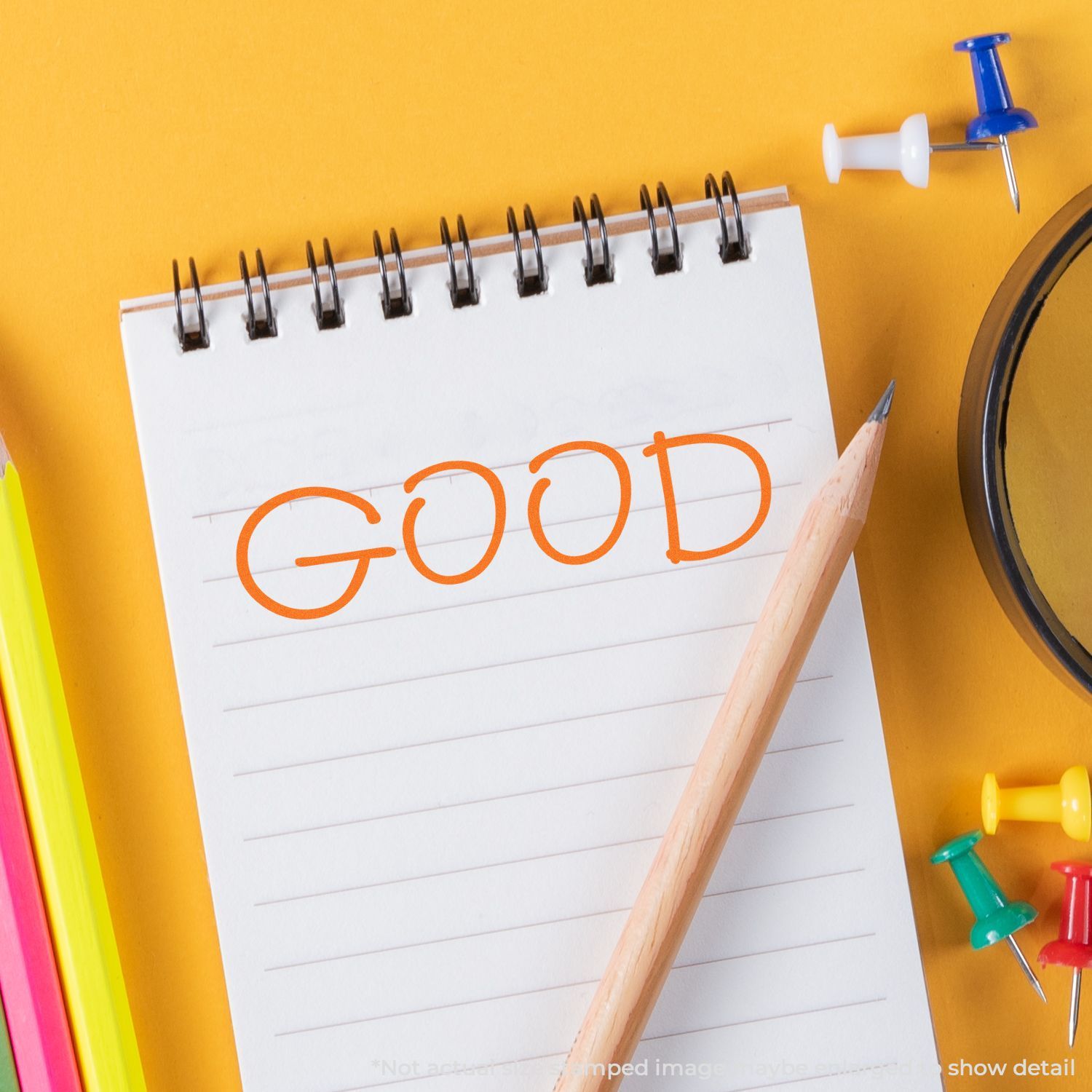 Notebook with GOOD written on it, pencil, and colorful push pins on a yellow background.