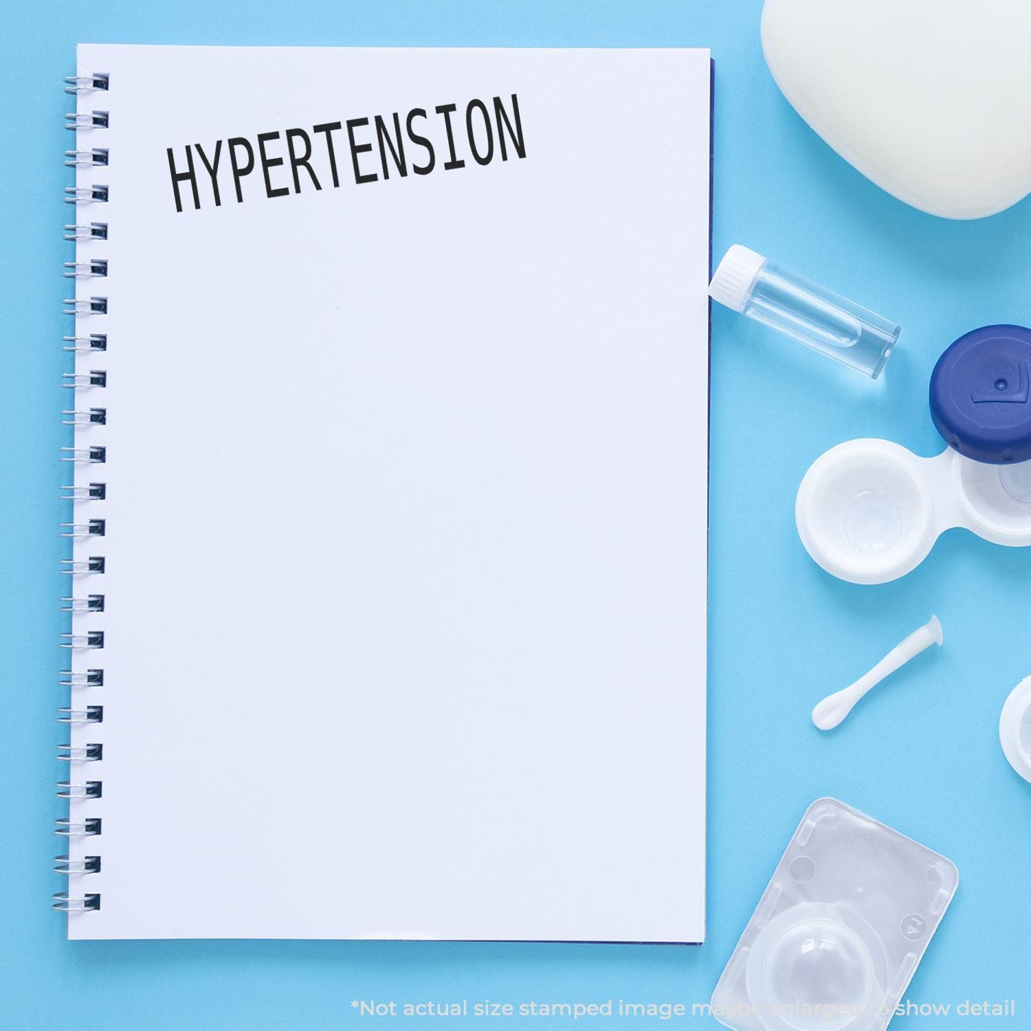 Hypertension education concept: blank notebook titled HYPERTENSION with medical tools on blue background.