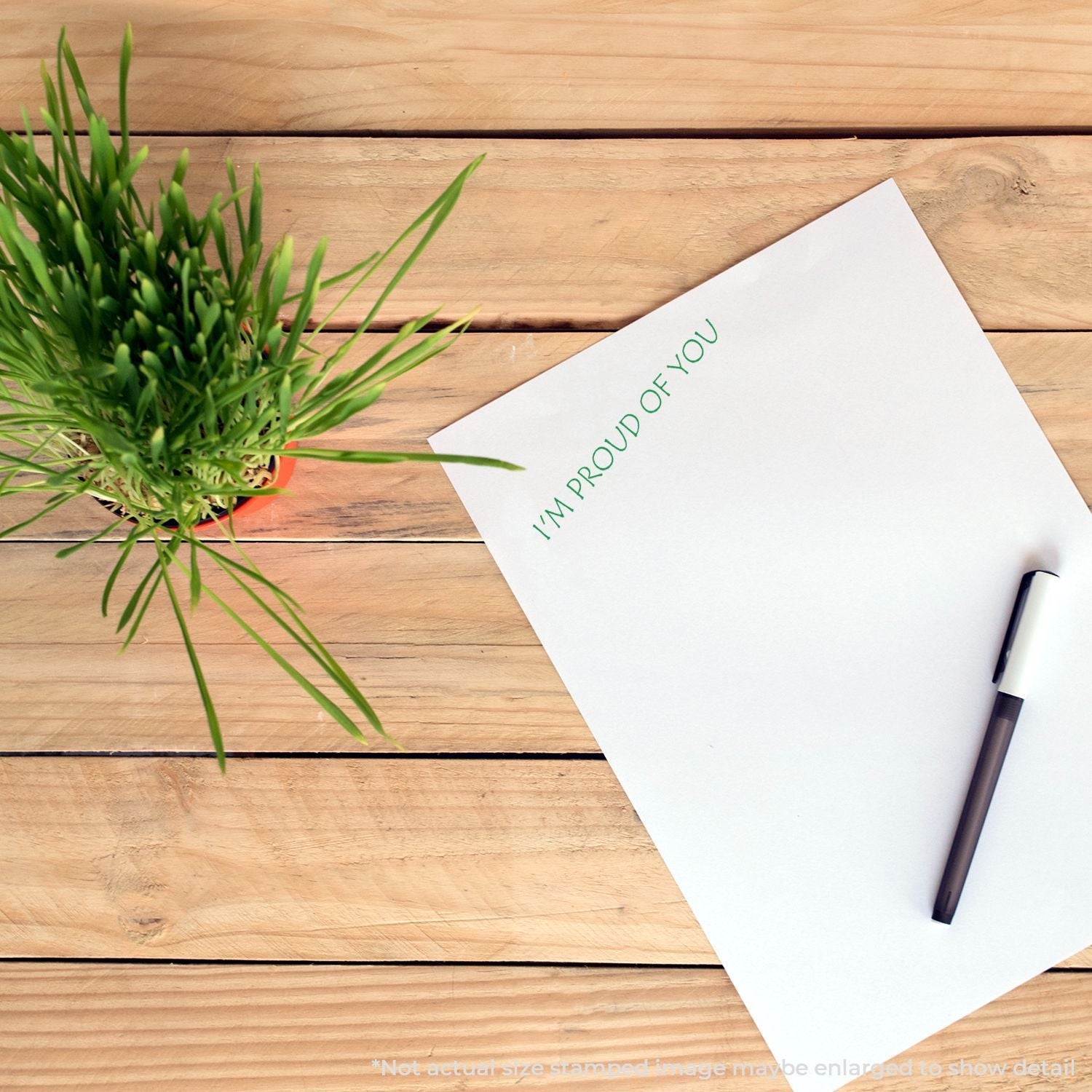 Motivational greeting card reading Im proud of you on wooden desk with pen and green plant