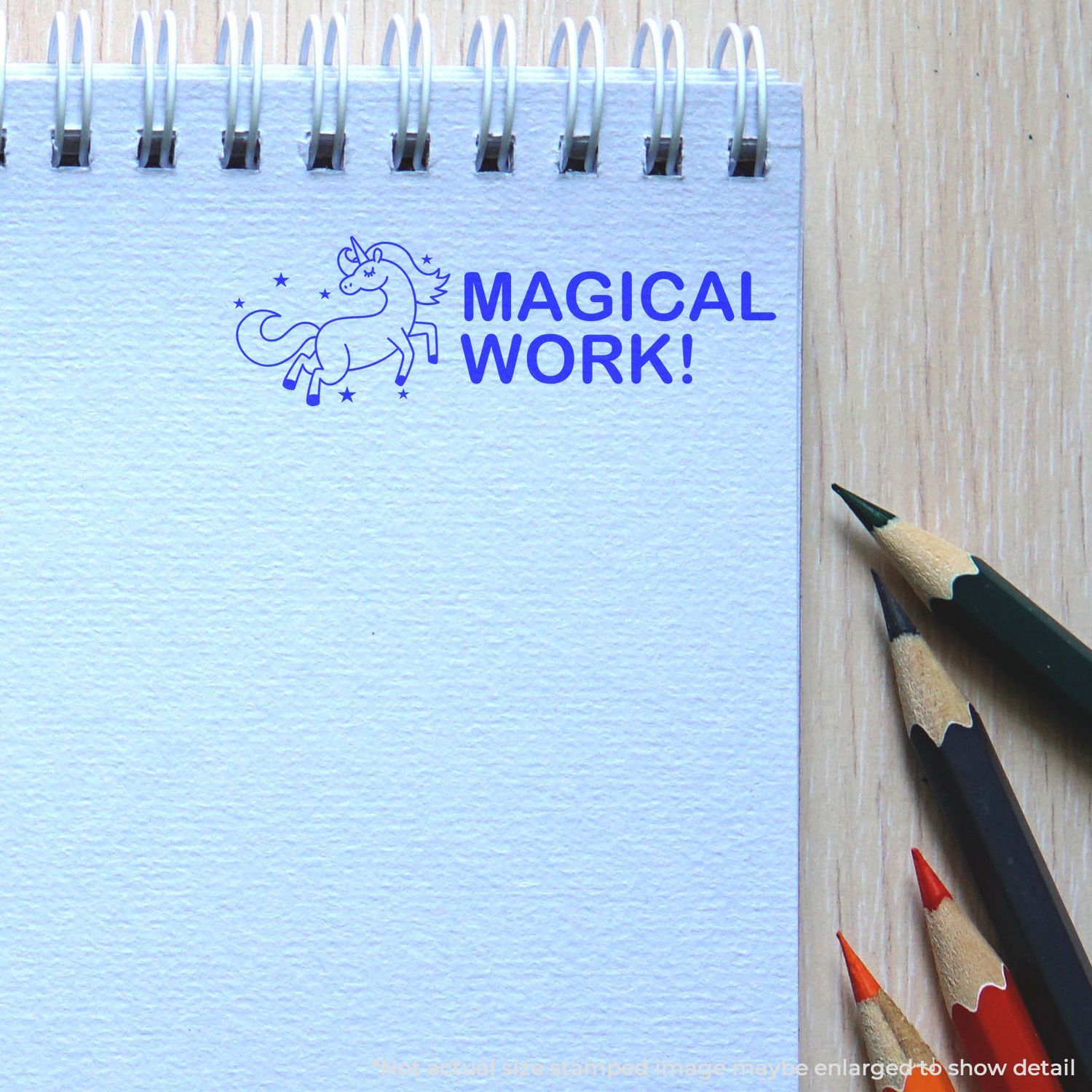 Notebook with Magical Work! unicorn logo and colored pencils on wooden desk, creative stationery flat lay.