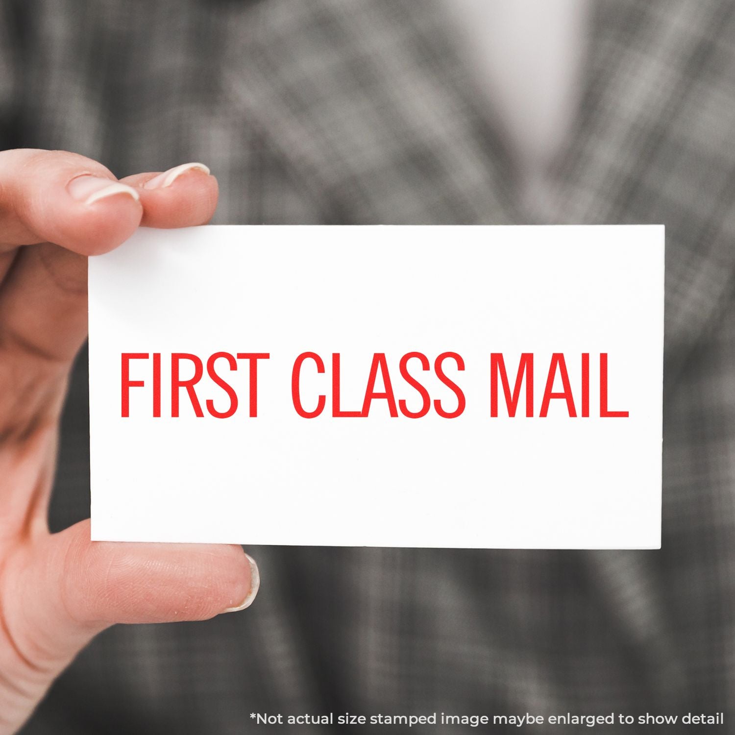 Hand holding a white first class mail card with bold red text on a blurred background.