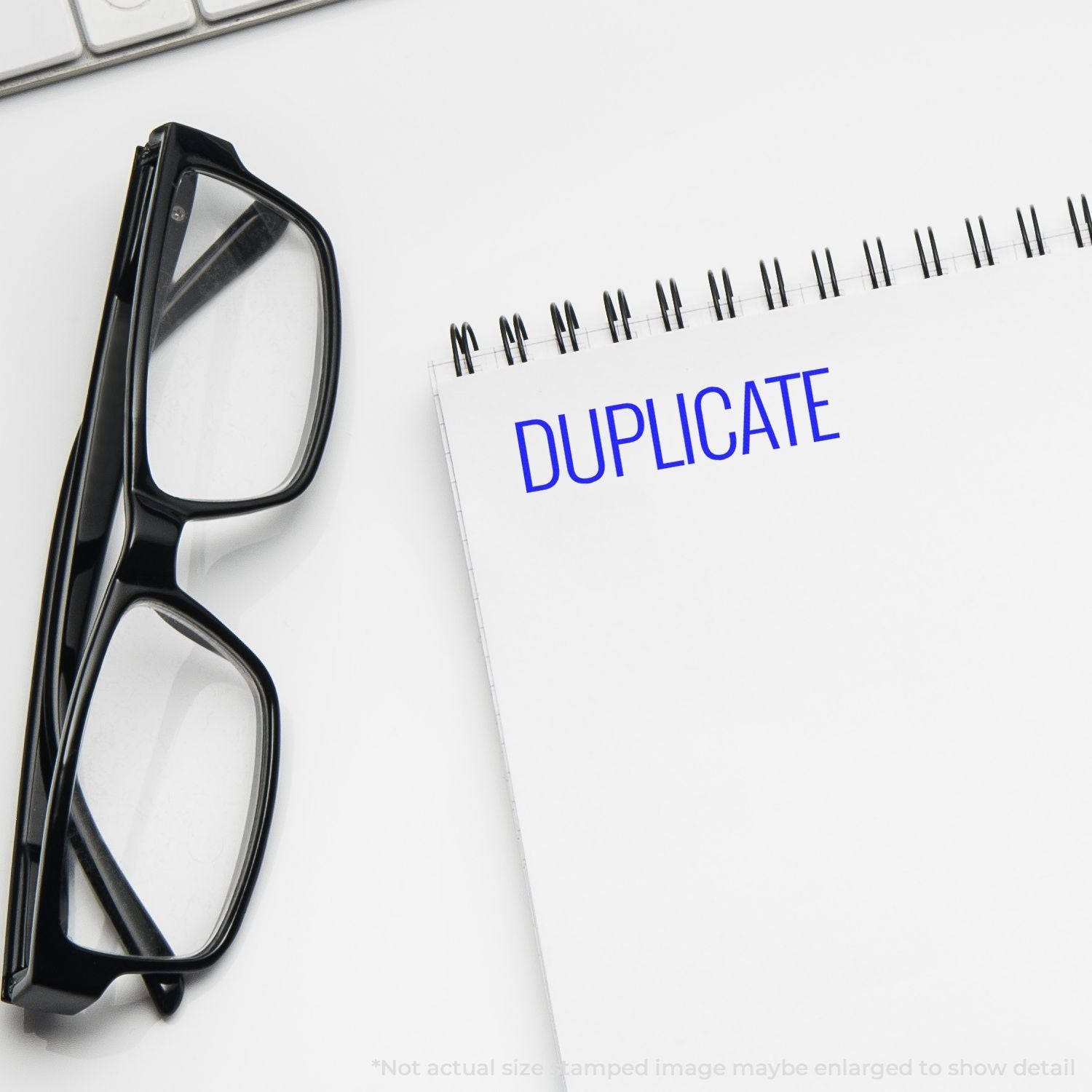Black eyeglasses beside a spiral notebook labeled duplicate on a white desk, office concept image.