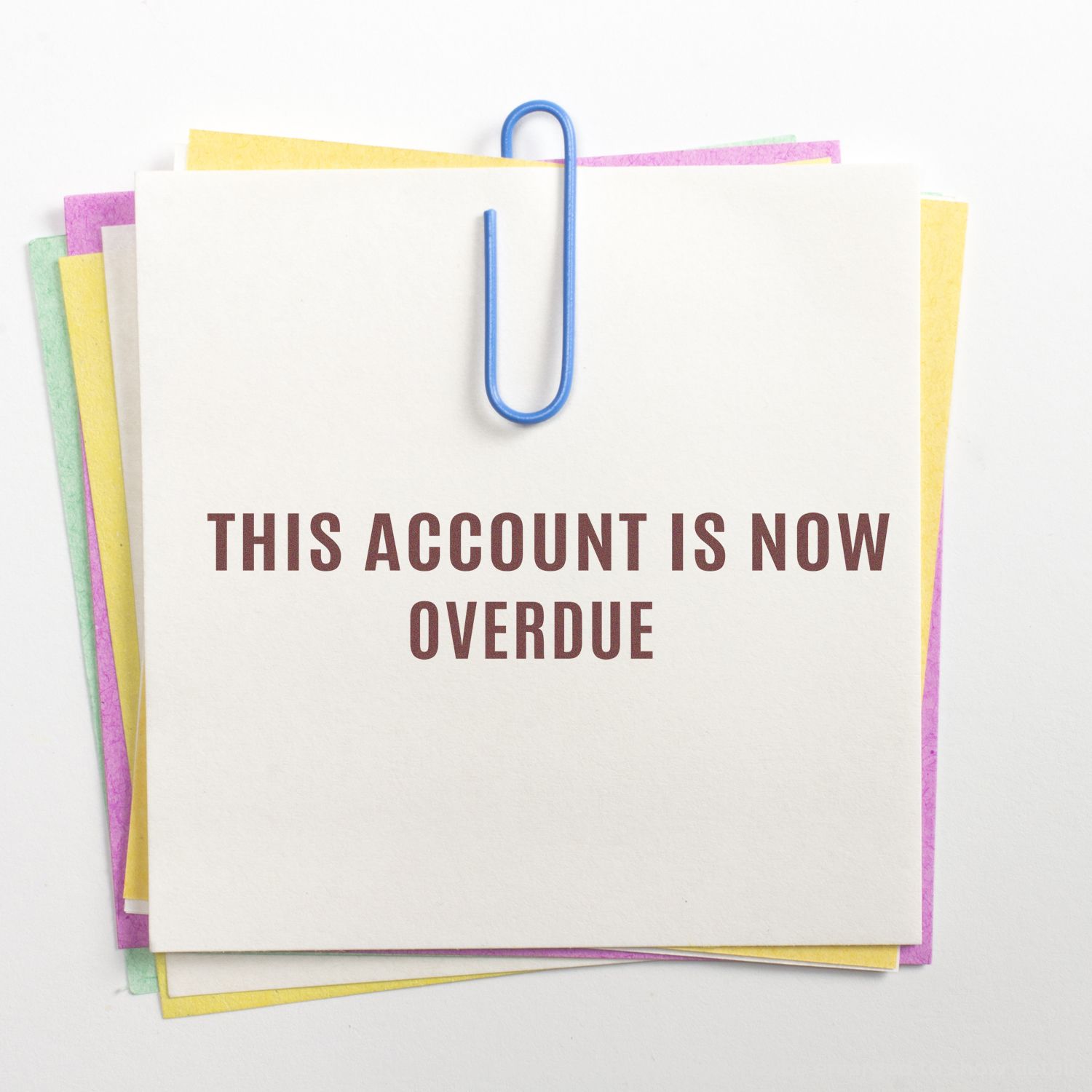 Overdue account notice on stacked paper documents clipped with blue paperclip, financial reminder warning.