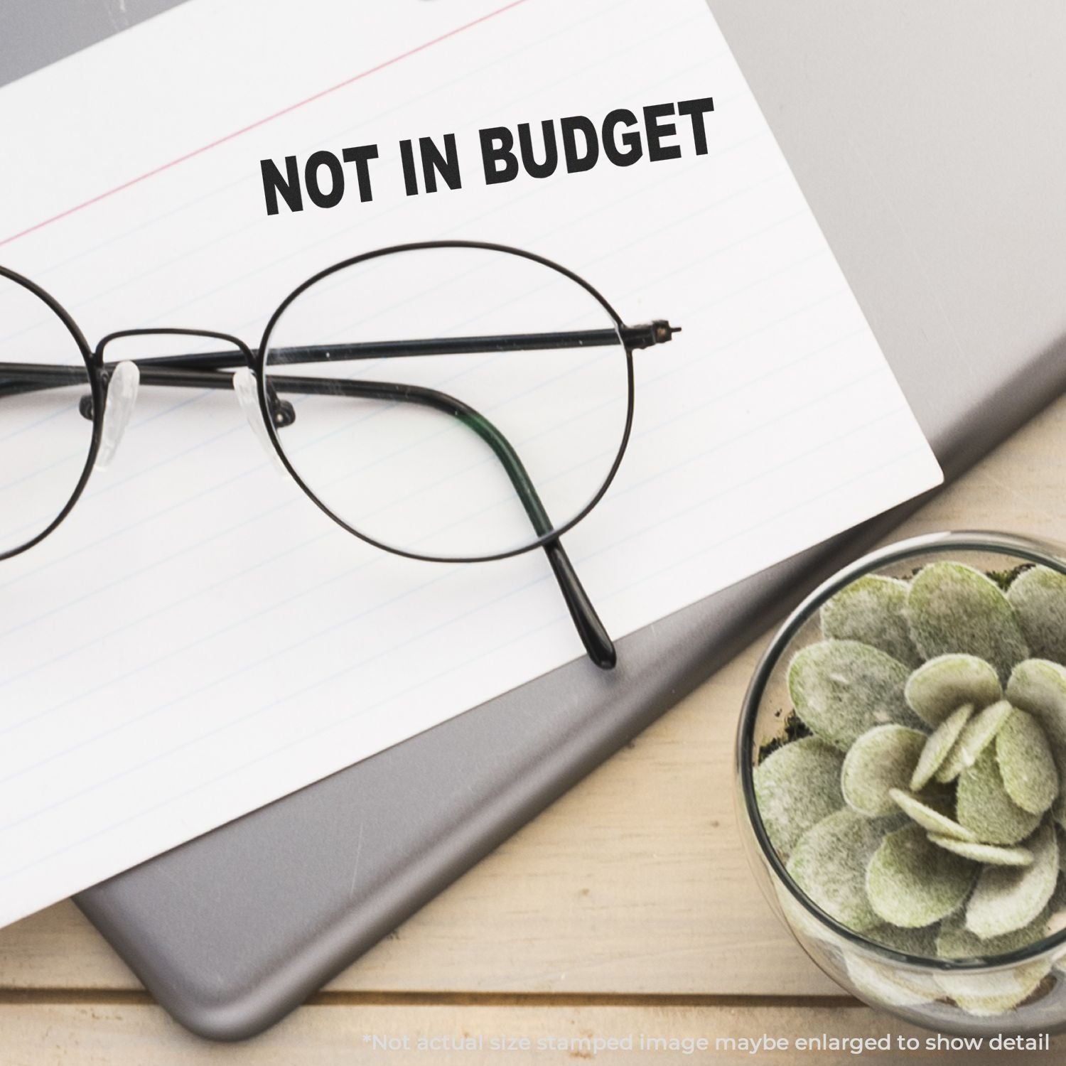 Round eyeglasses on a notebook labeled Not in Budget beside a small succulent on a desk, concept of budget planning and expensive purchases