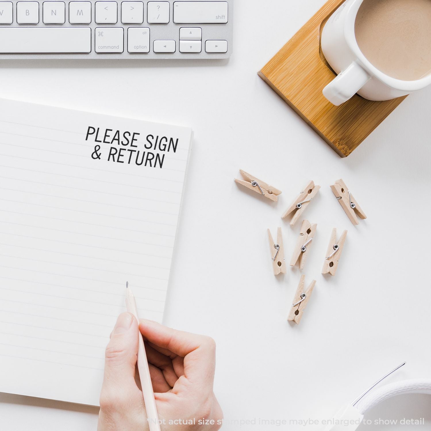 Hand holding pen writing Please sign & return on a document with coffee, keyboard, and clothespinssignature request