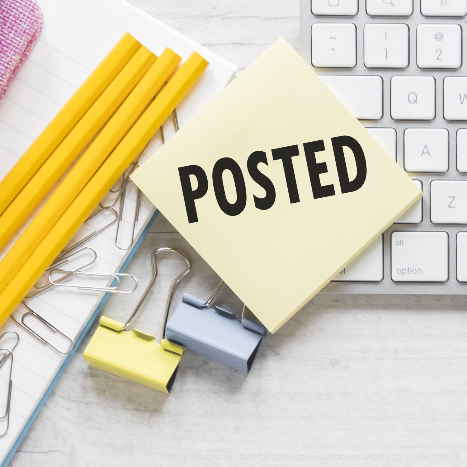 Sticky note with POSTED on office desk beside keyboard, notebook, paper clips, and yellow pencils.