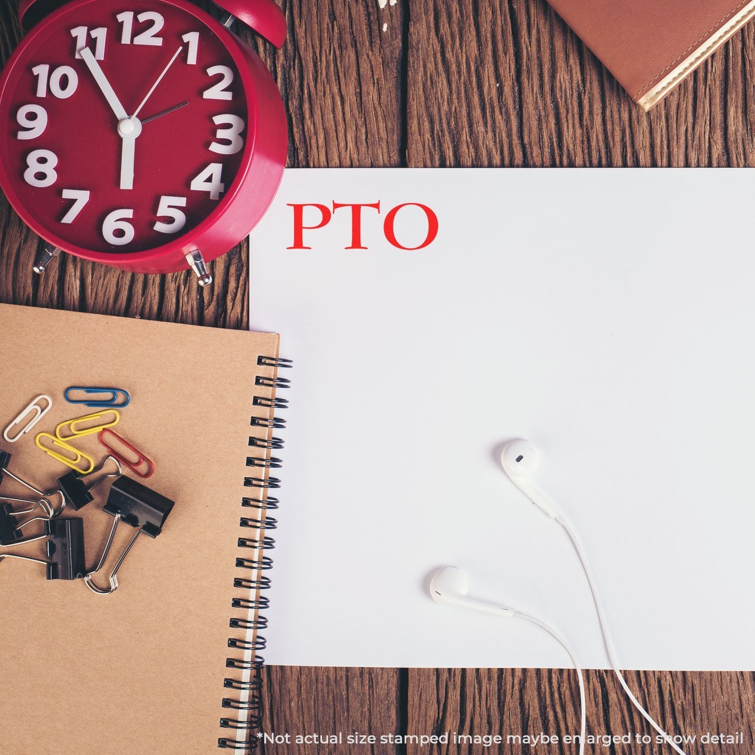 Red alarm clock beside notebook labeled PTO with paper clips and white earphones on wooden desk for time management