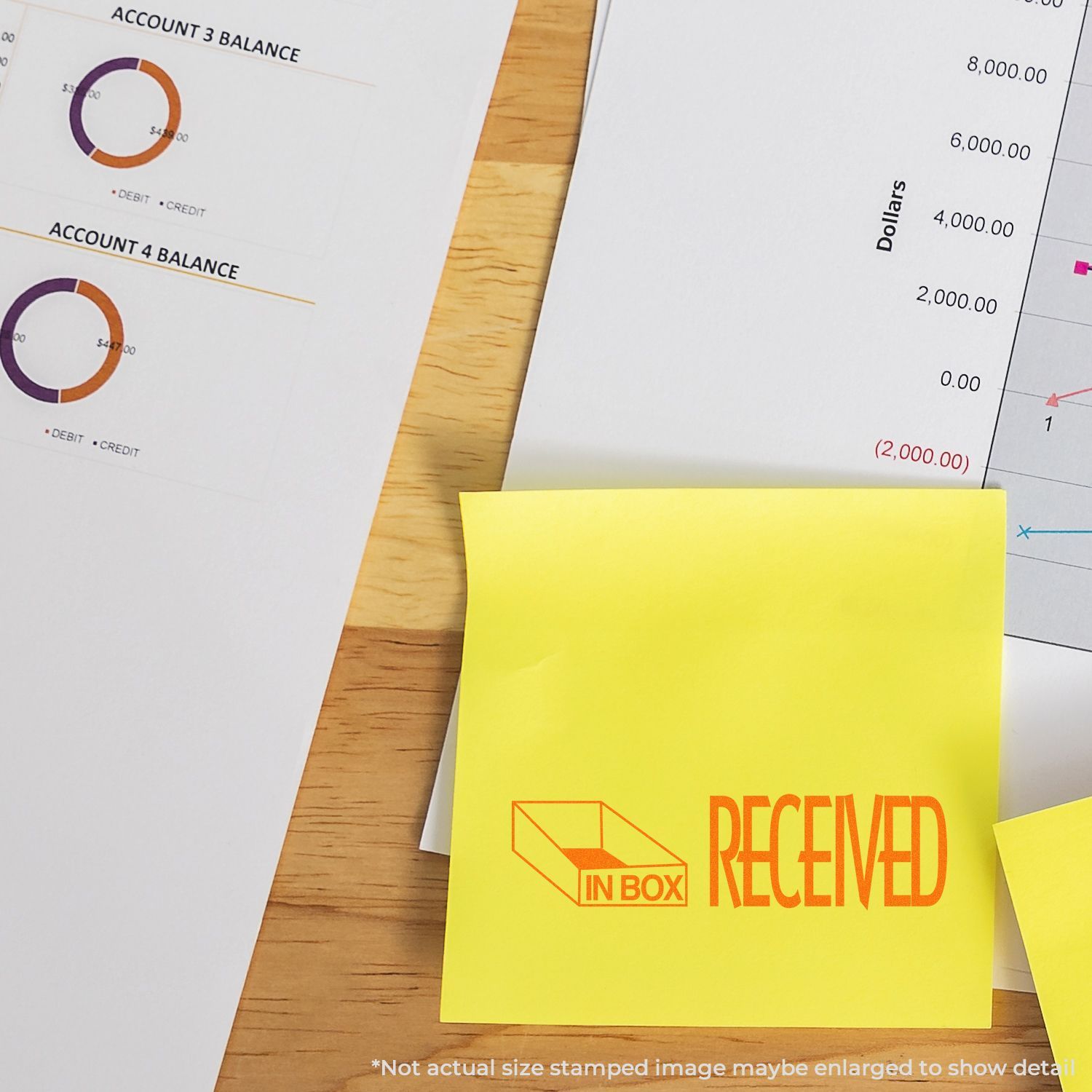 Yellow sticky note with Received in-box stamp on accounting reports and financial balance charts on a wooden desk.