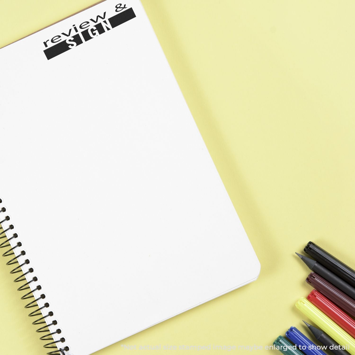 Review & Sign notebook with pens and pencils on a yellow desk, promoting document review and signature workflow.