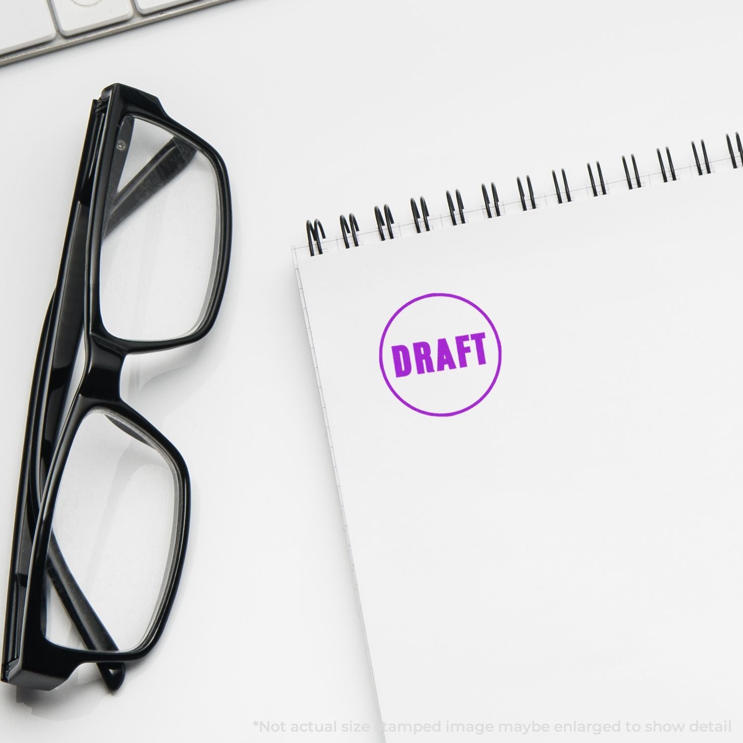 Black eyeglasses beside a spiral notebook stamped DRAFT on a clean white desk, office workspace concept.