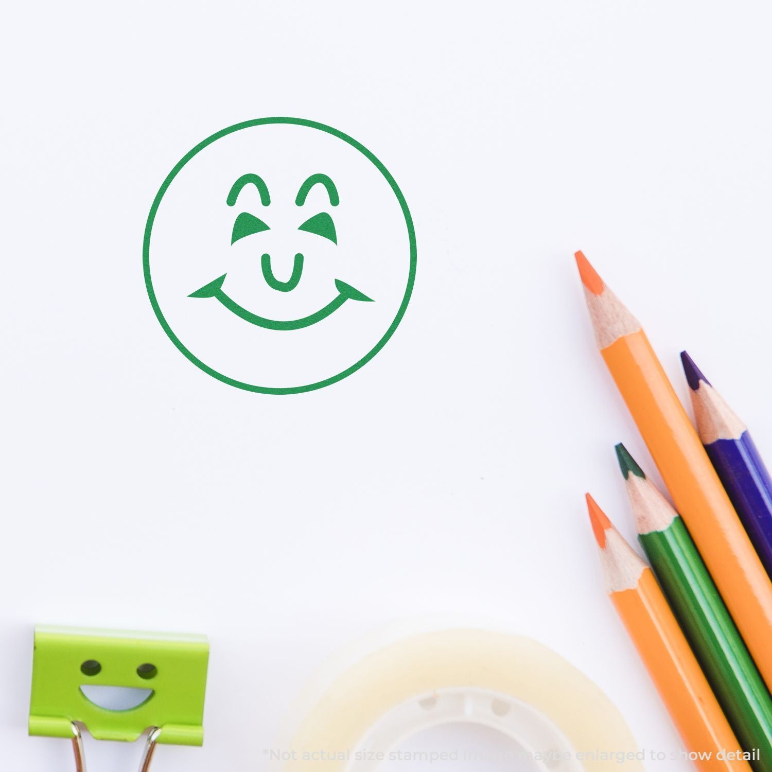 Green smiley face stamp on white paper with colorful pencils, creative school supplies close-up.
