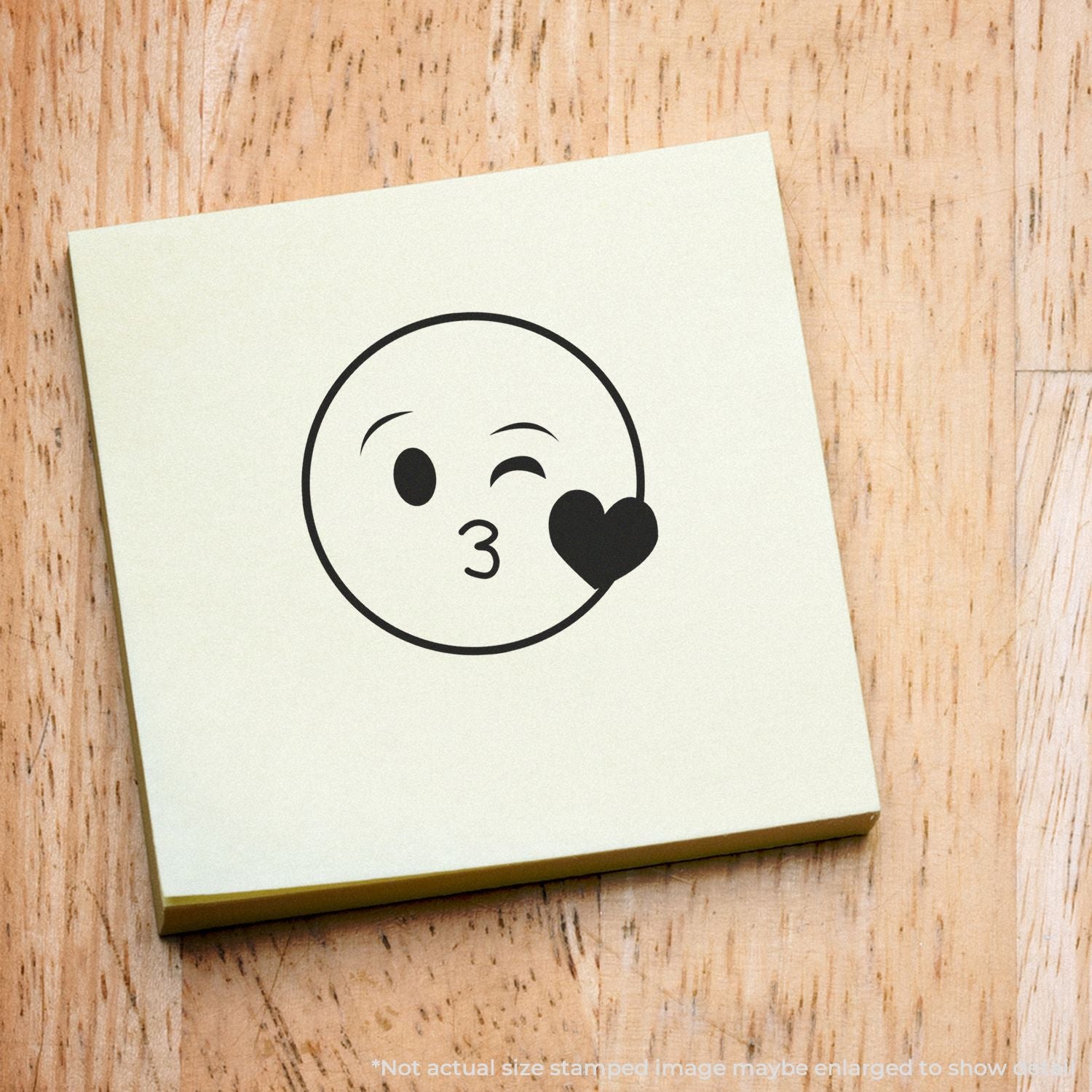 Winking kiss emoji with heart icon on a square sticky note mockup on a wooden background