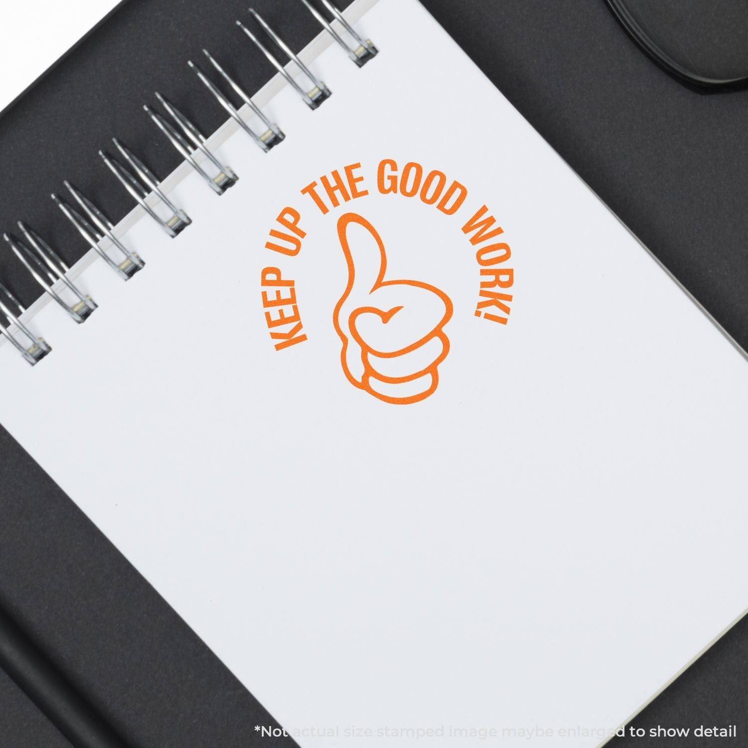Orange Keep Up the Good Work spiral notebook with thumbs-up design on a dark desk background