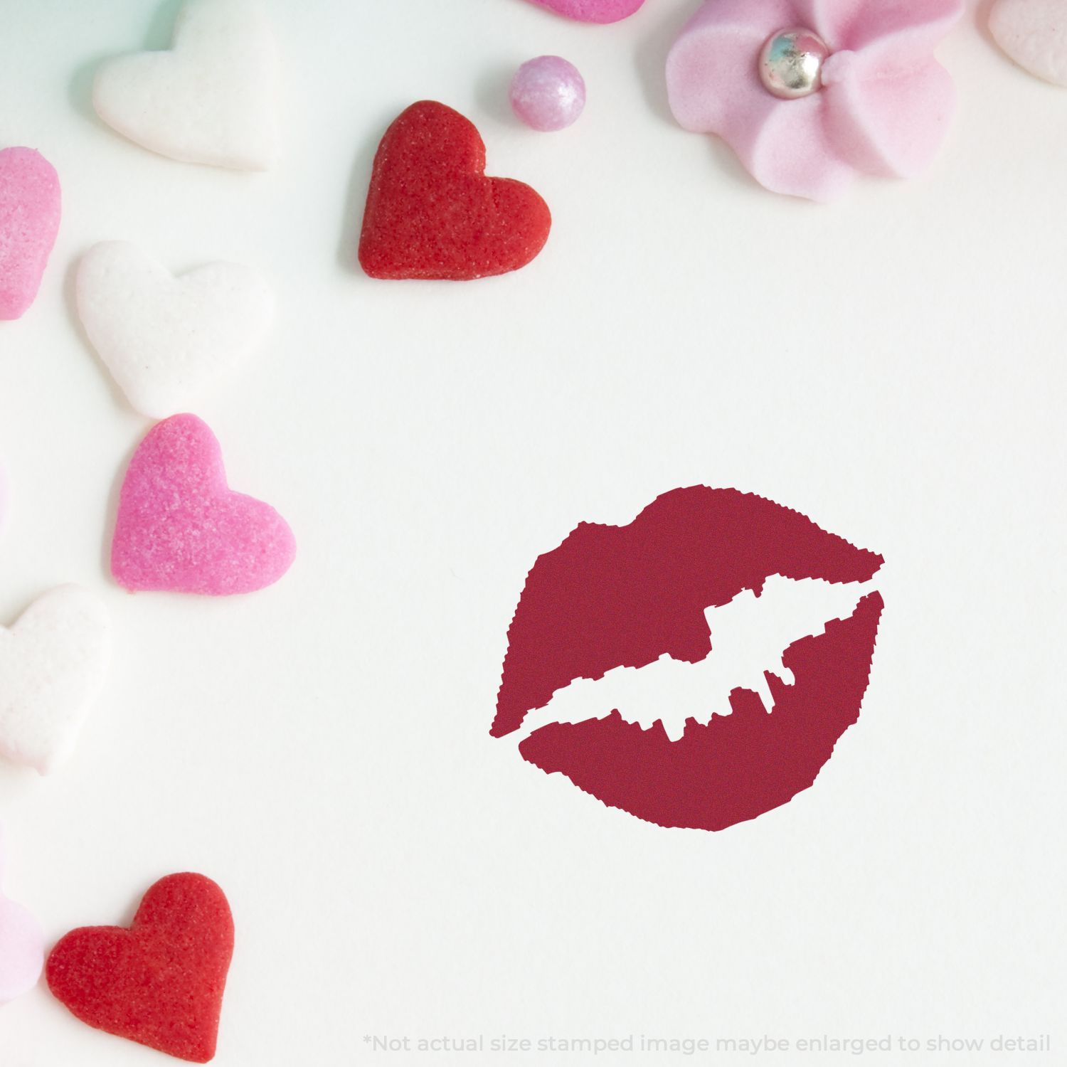 Red lipstick kiss print surrounded by pink and red heart candies on a white background, romantic Valentines Day theme.
