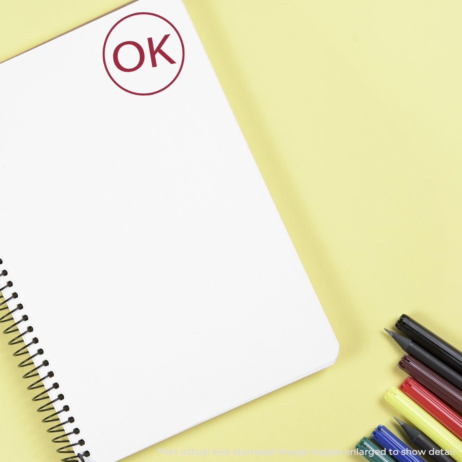 Blank spiral notebook with OK stamp and colorful markers on yellow background