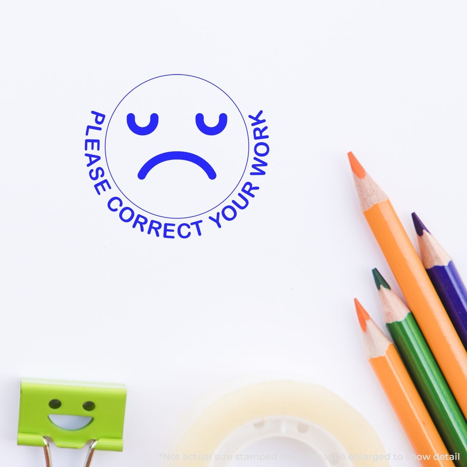 Please correct your work stamp with sad face on white paper, alongside colorful pencils and a binder clip.