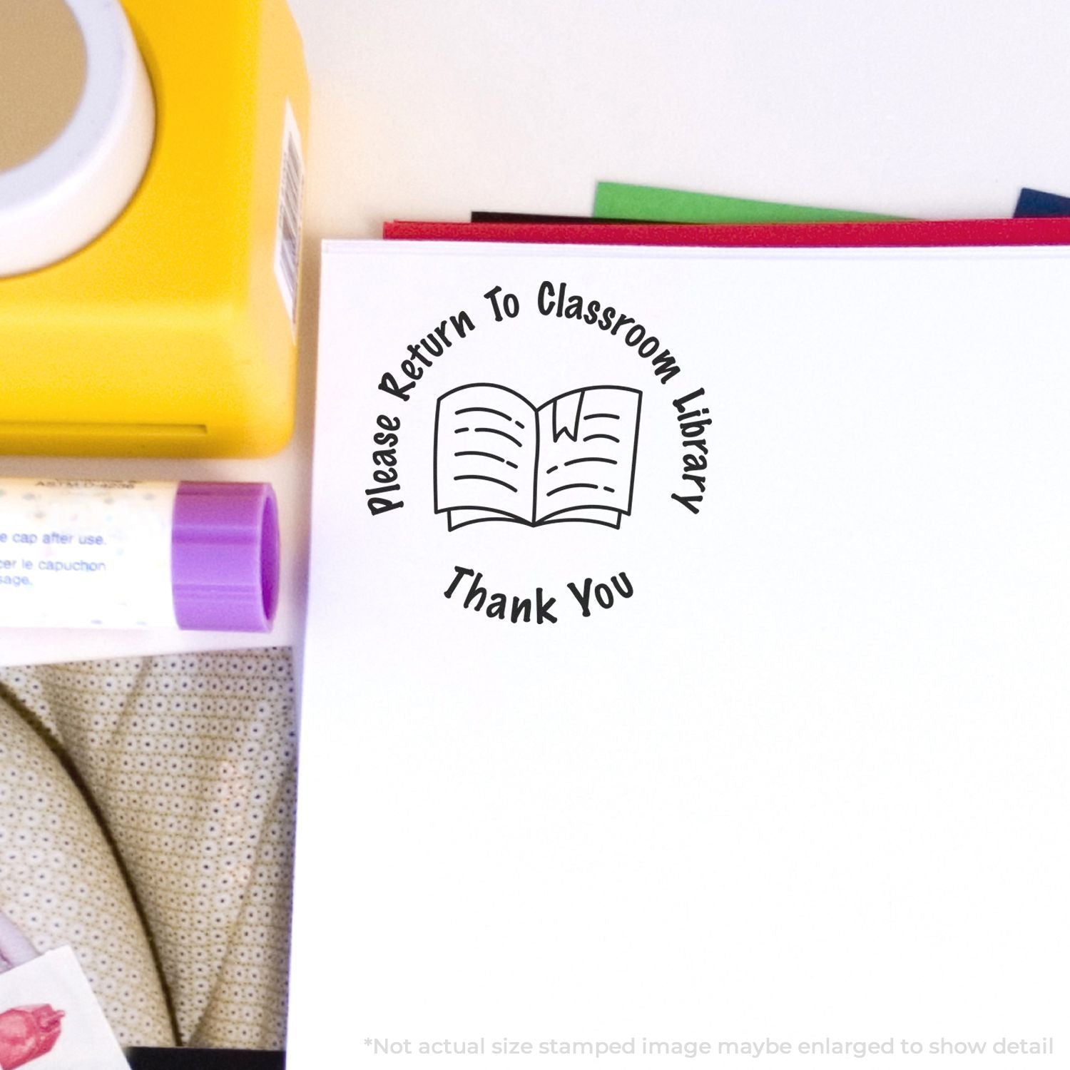 Classroom library return stamp with open book icon and Please Return to Classroom Library Thank You text on paper, next to school supplies.