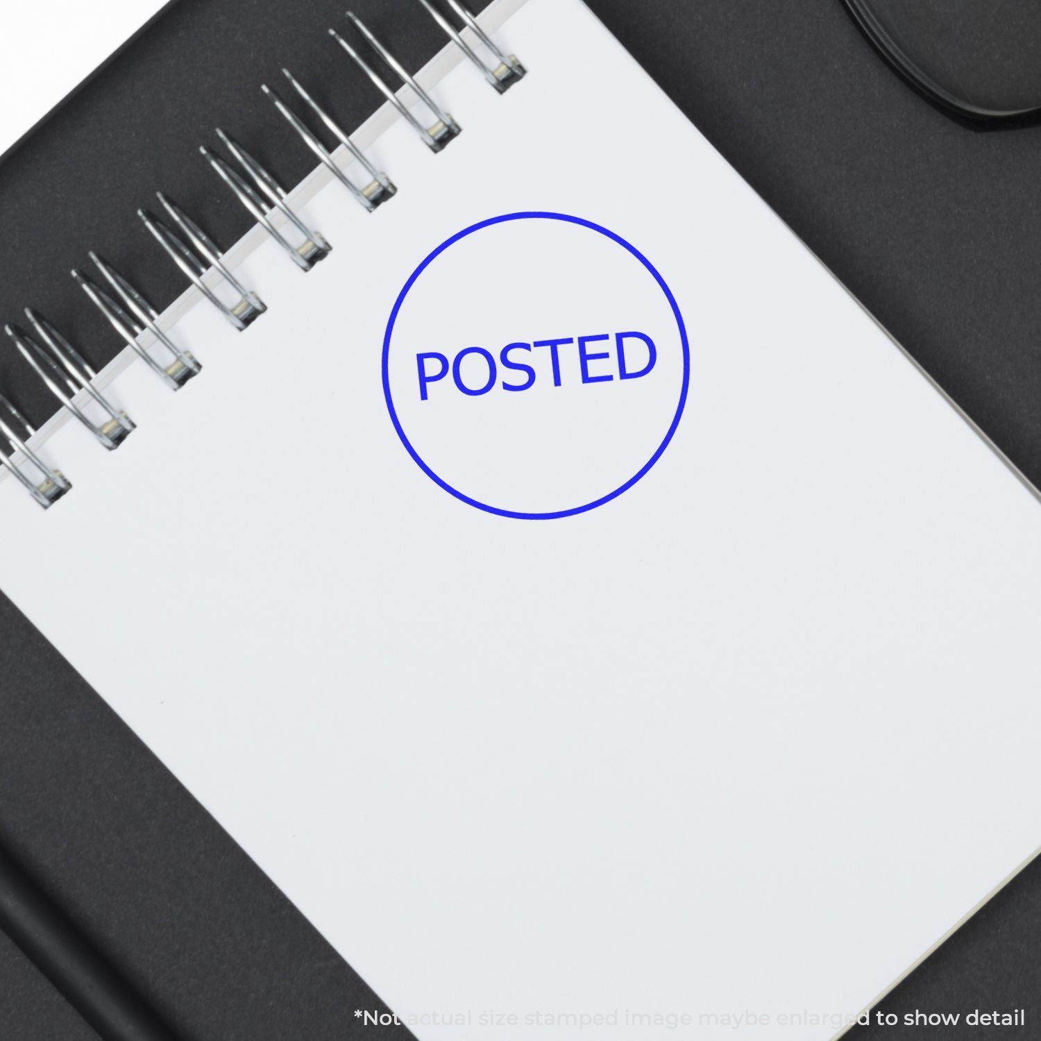 Blank spiral notebook with blue POSTED stamp on white paper, office stationery close-up.