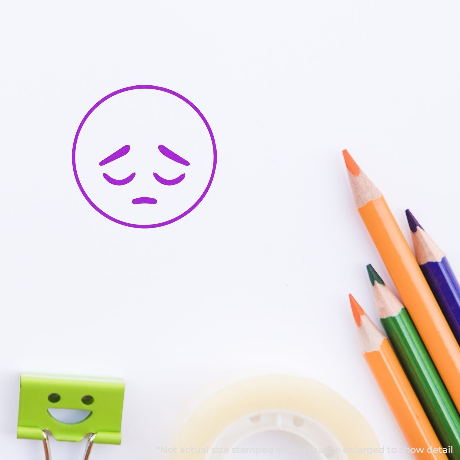 Sad purple emoticon drawn on white paper with colored pencils and a smiley binder clip on a clean workspace background