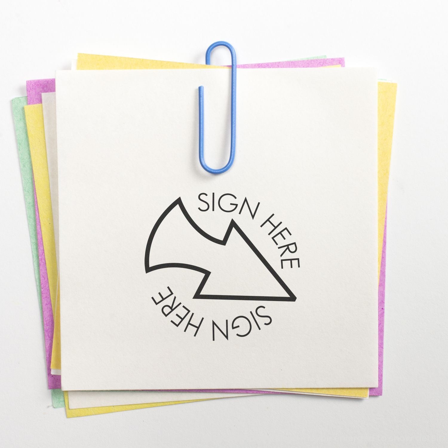 Stack of pastel sticky notes clipped with a blue paperclip, featuring a sign here arrow symbol on white paper.
