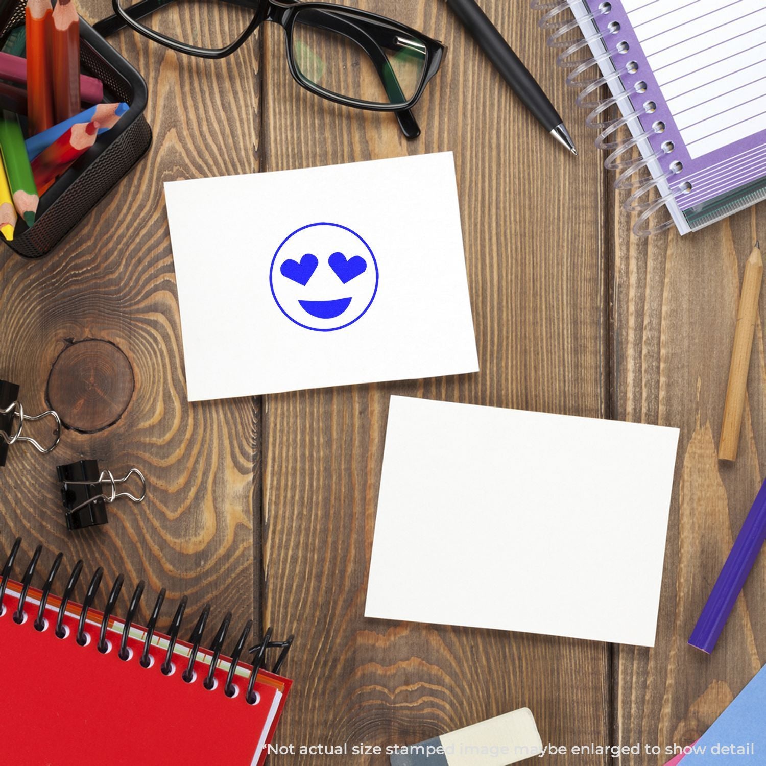 Flat lay of back-to-school supplies on a wooden desk with a heart-eyes smiley on a blank note, pencils, glasses, pen, and spiral notebooks.