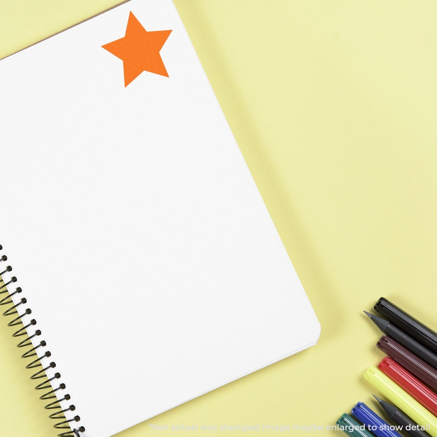 Blank spiral notebook with orange star sticker and colorful markers on a yellow background for creative writing and school supplies.