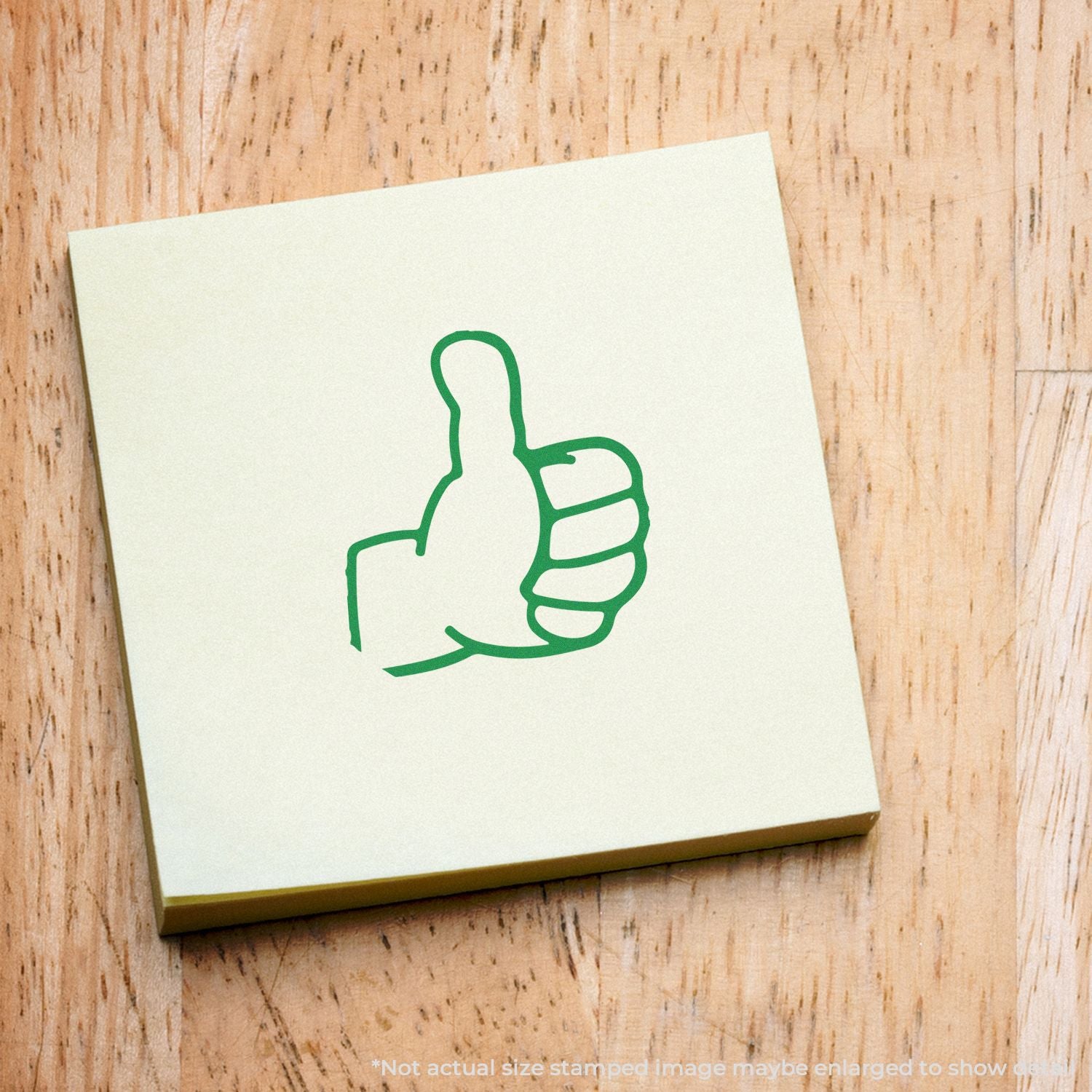 Green thumbs-up logo on a sticky note pad placed on a wooden desk surface.