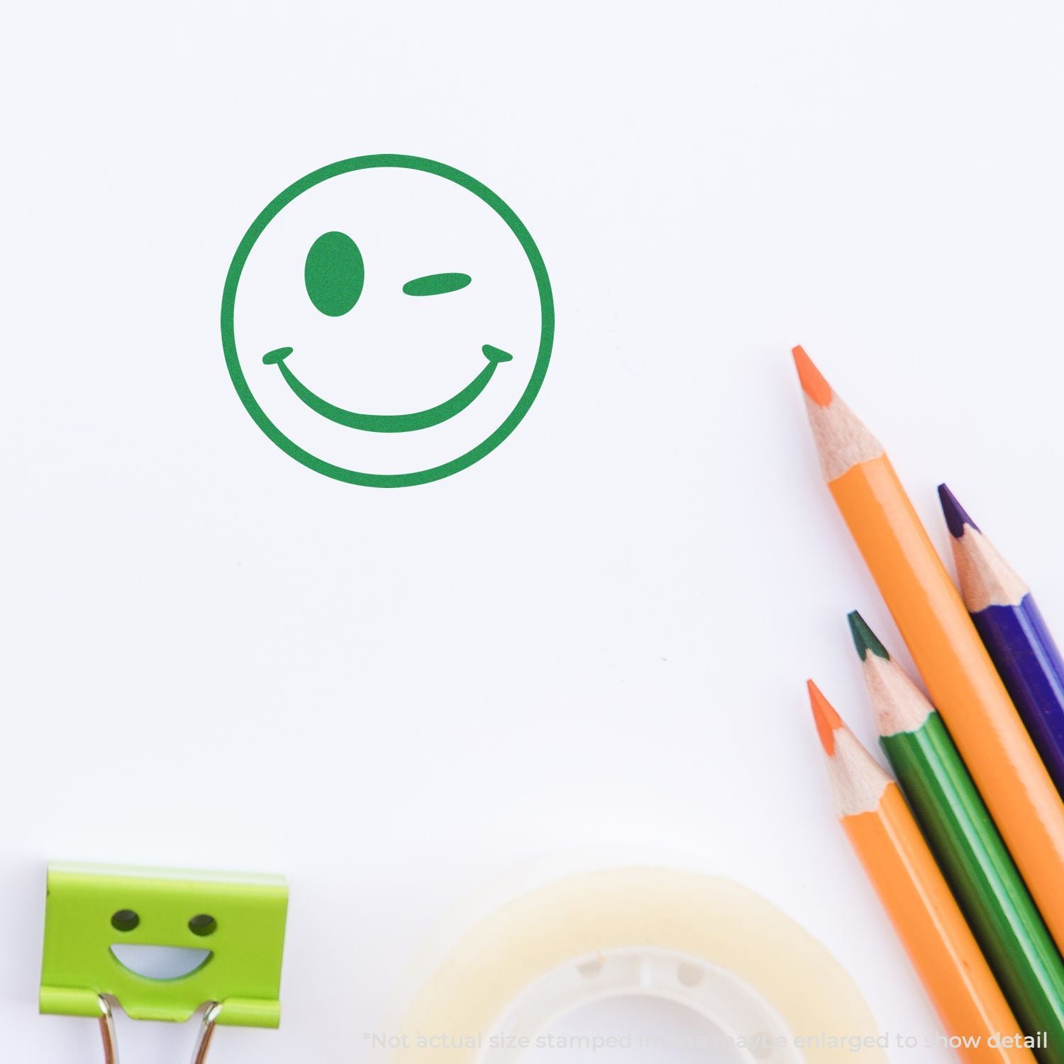Green smiley face stamp on white paper with colorful pencils, creative stationery and school supply concept.