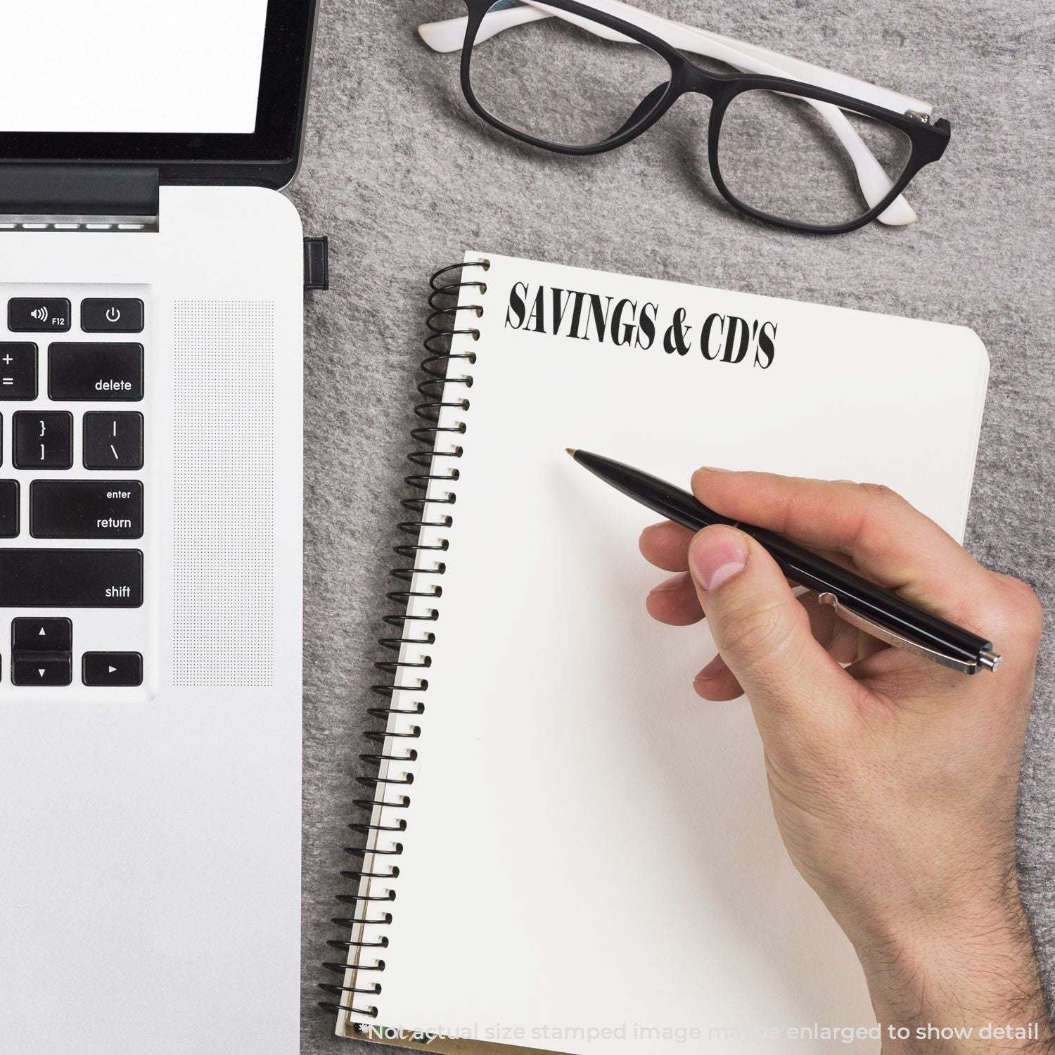 Hand writing savings and CDs notes beside a laptop and eyeglasses on a desk, personal finance planning concept.