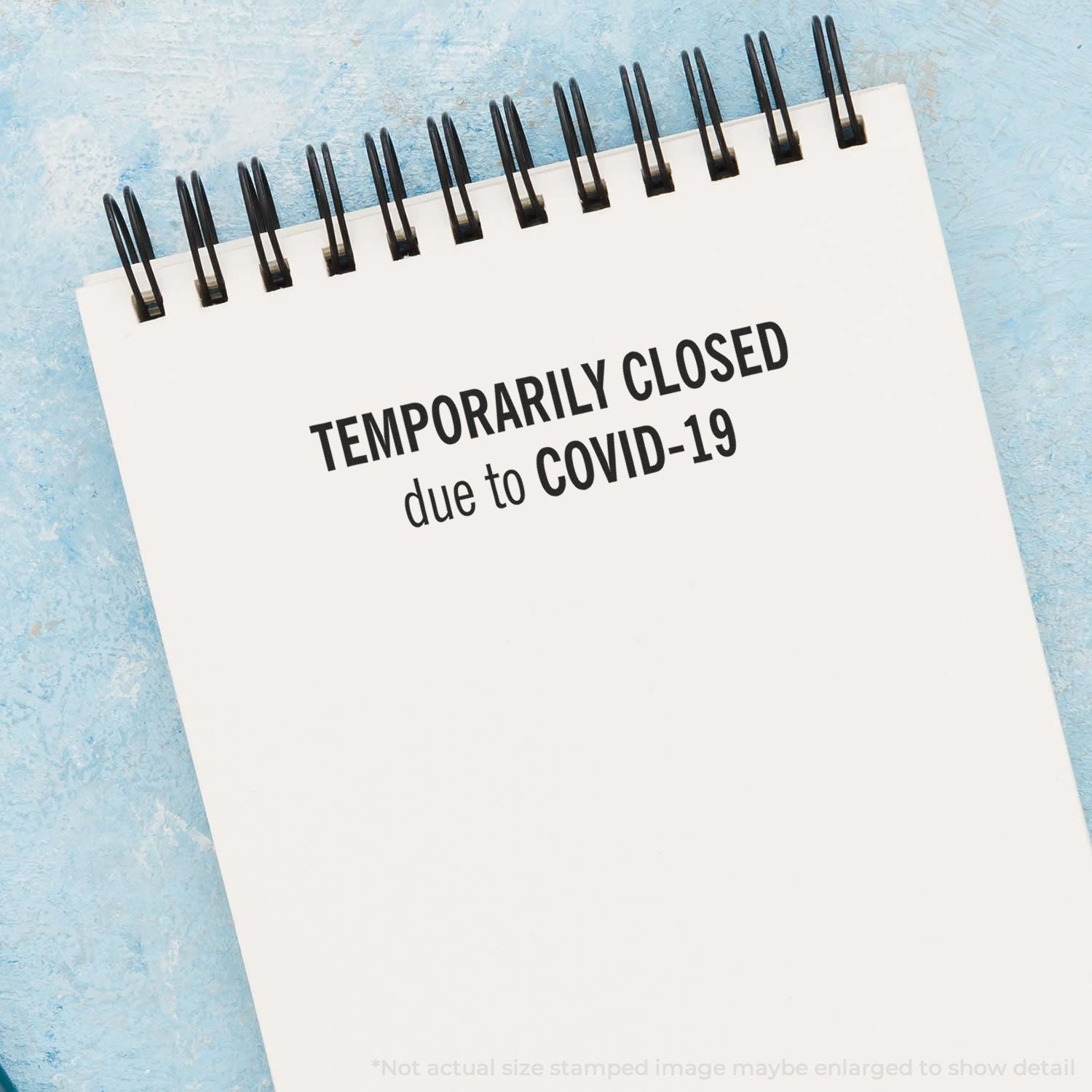 Notepad with Temporarily Closed due to COVID-19 message on blue background, business closure announcement during coronavirus pandemic.